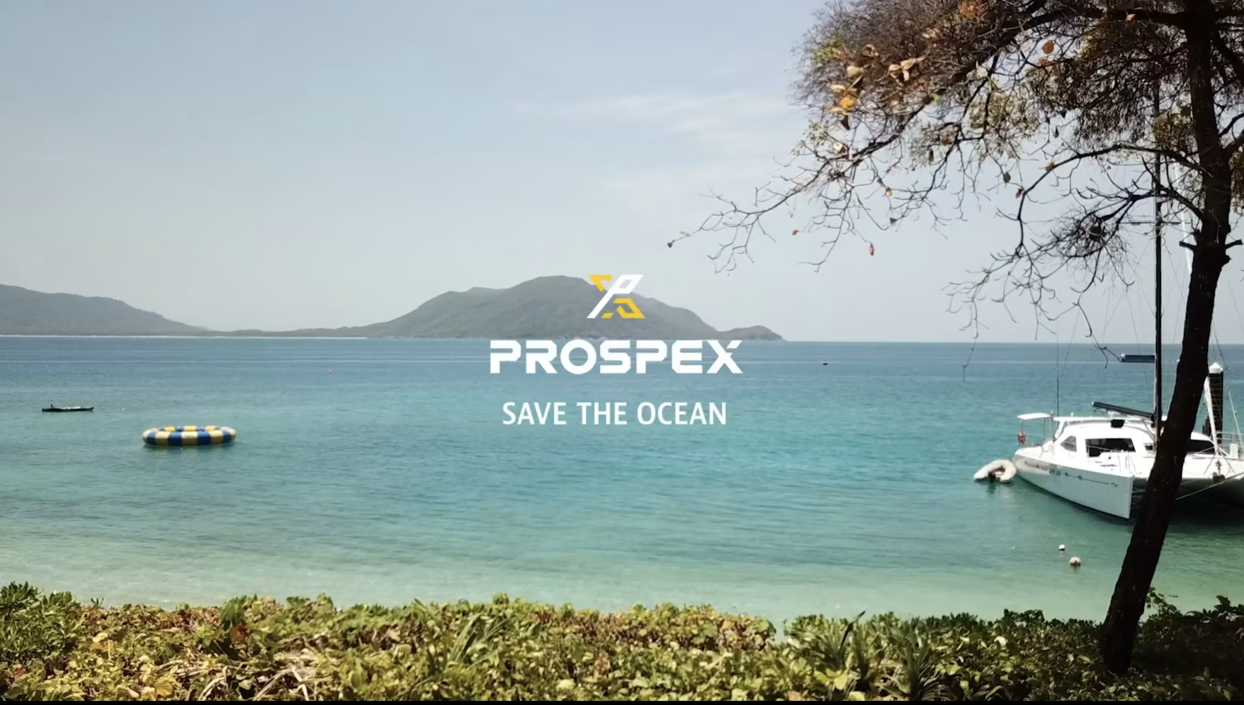 A peaceful ocean scene with clear turquoise water, a sailboat docked near the shore, and a small floating ring. There are distant islands and a partly cloudy sky. The image features the PROSPEX logo with the phrase "SAVE THE OCEAN."