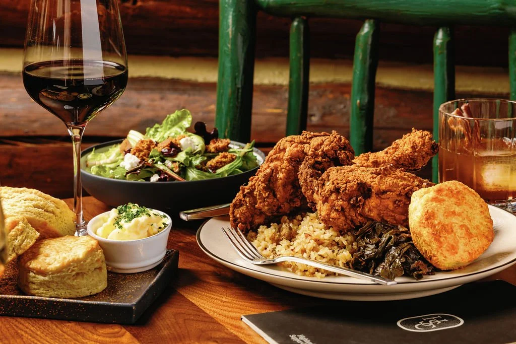 Fried chicken with rice, salad, cornbread, mashed potatoes, and a glass of red wine on a wooden table.