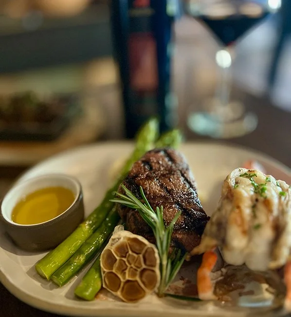 Steak with asparagus, mashed potatoes, garlic, and a side of olive oil or sauce on a white plate