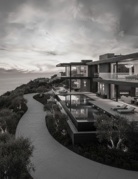 Modern multi-story house with outdoor pool, overlooking the ocean at sunset.