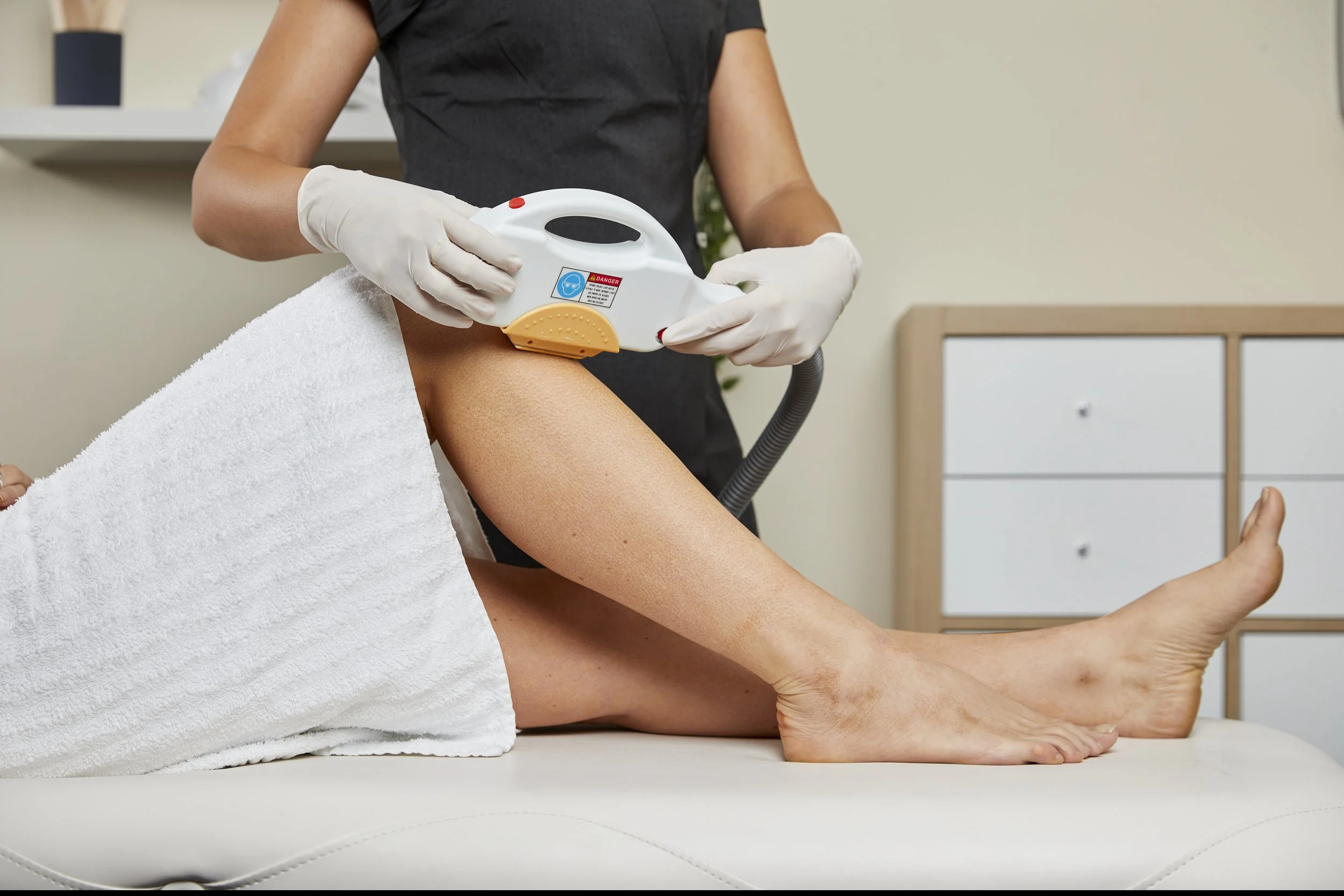 A woman receiving laser hair removal treatment on her leg in a medical clinic setting.