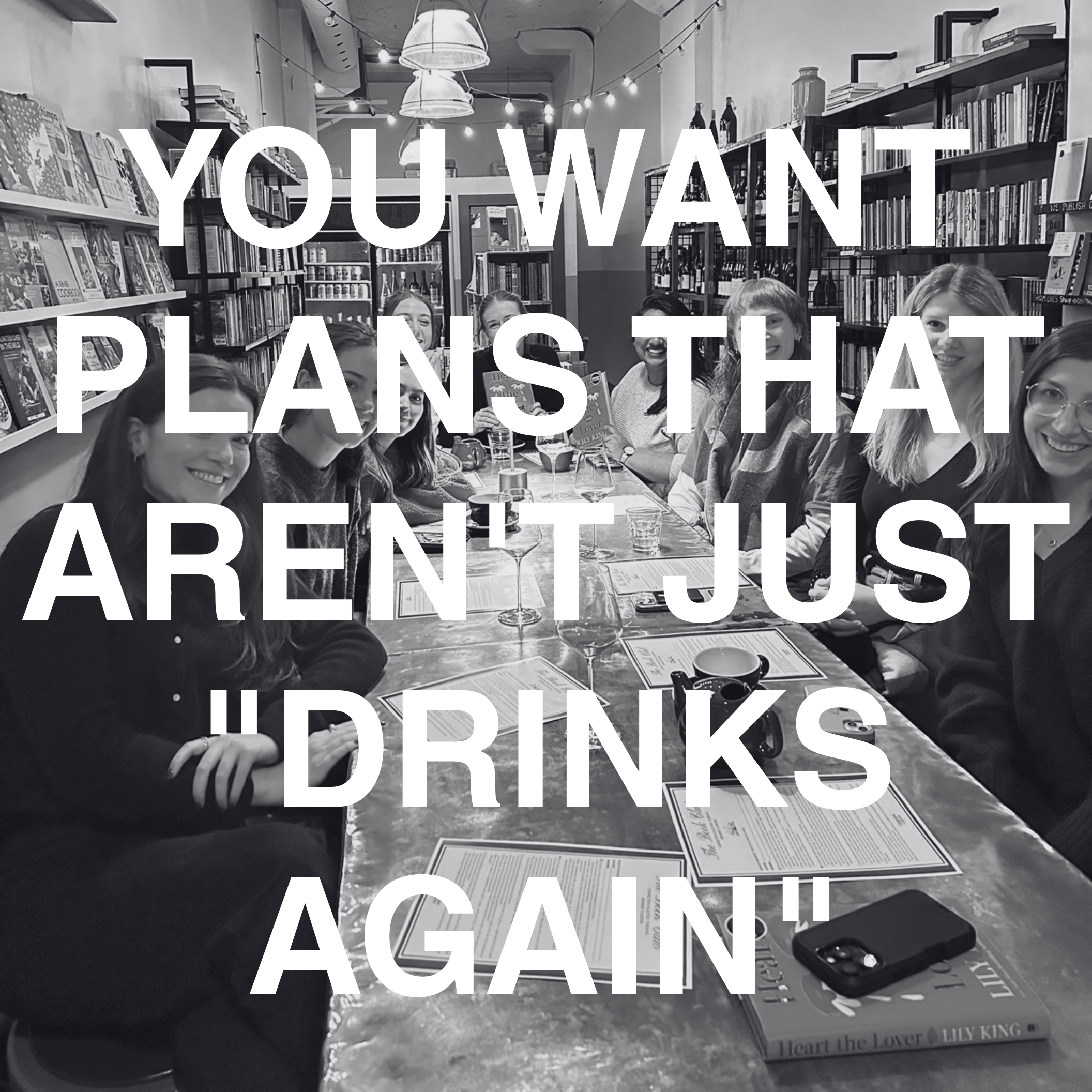 A group of women sitting at a long table in a bookstore or library, smiling, with drinks and menus in front of them. The room is decorated with bookshelves, hanging lights, and string lights, and there is a large, overlaid quote that reads, "You want plants that aren’t just drinks again."