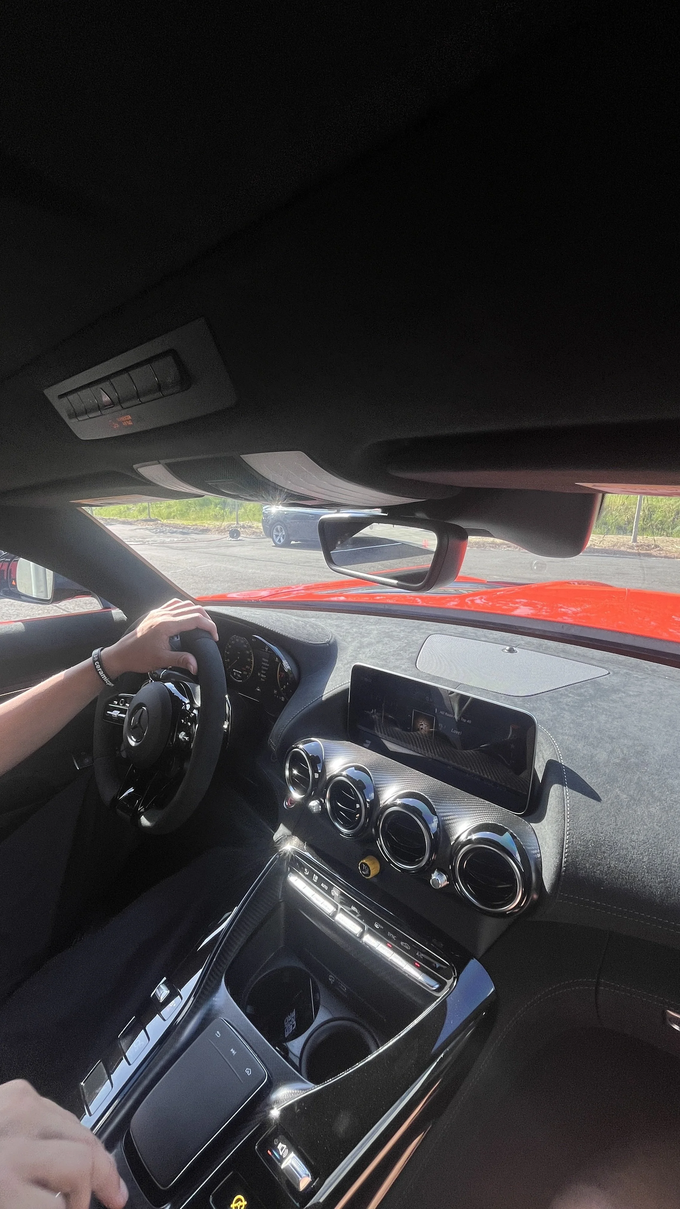 Inside view of a modern car dashboard with a person driving, showing a steering wheel, digital display, climate controls, and center console.