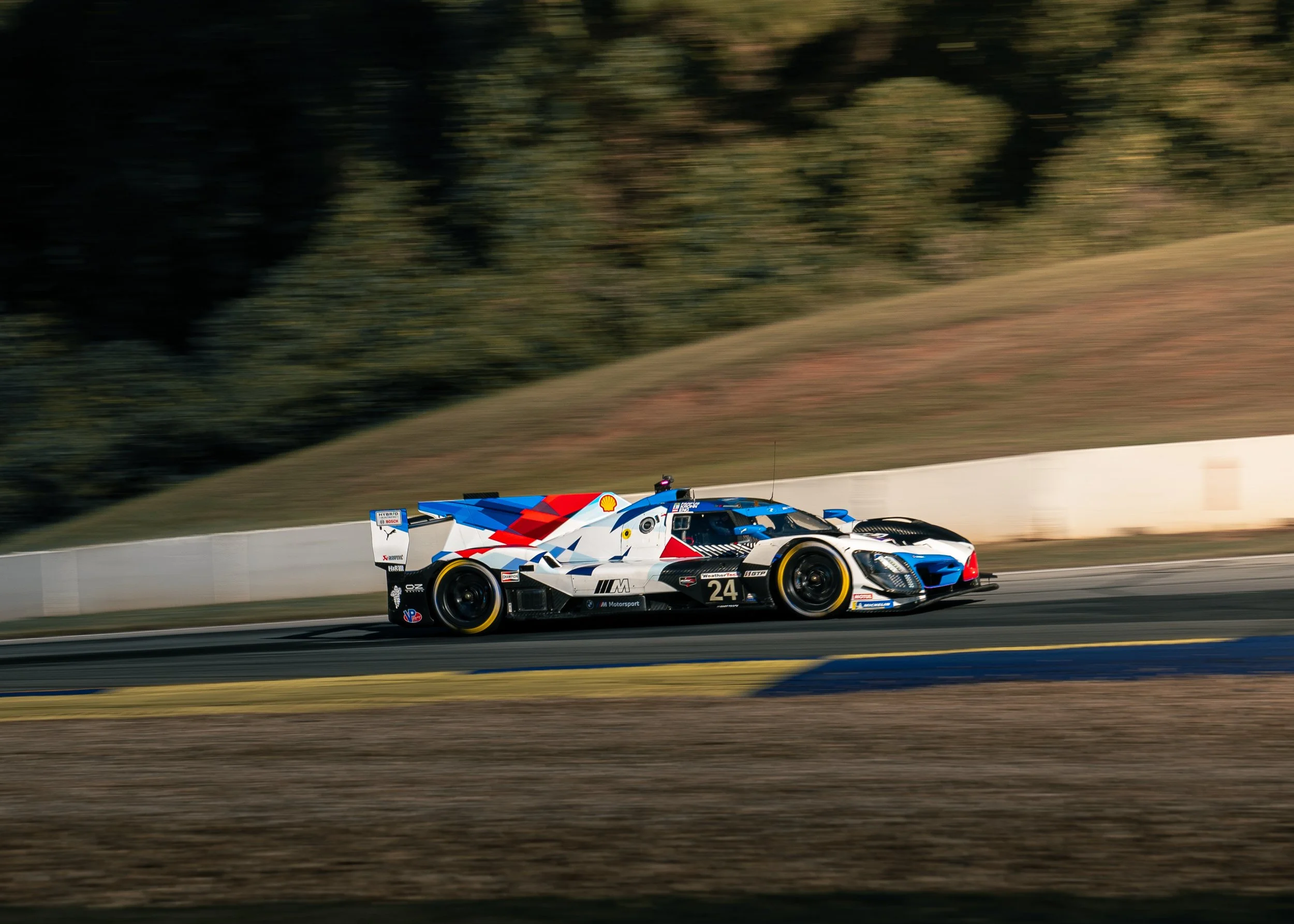 A race car with a blue, white, and red livery speeding on a race track with a blurred background.