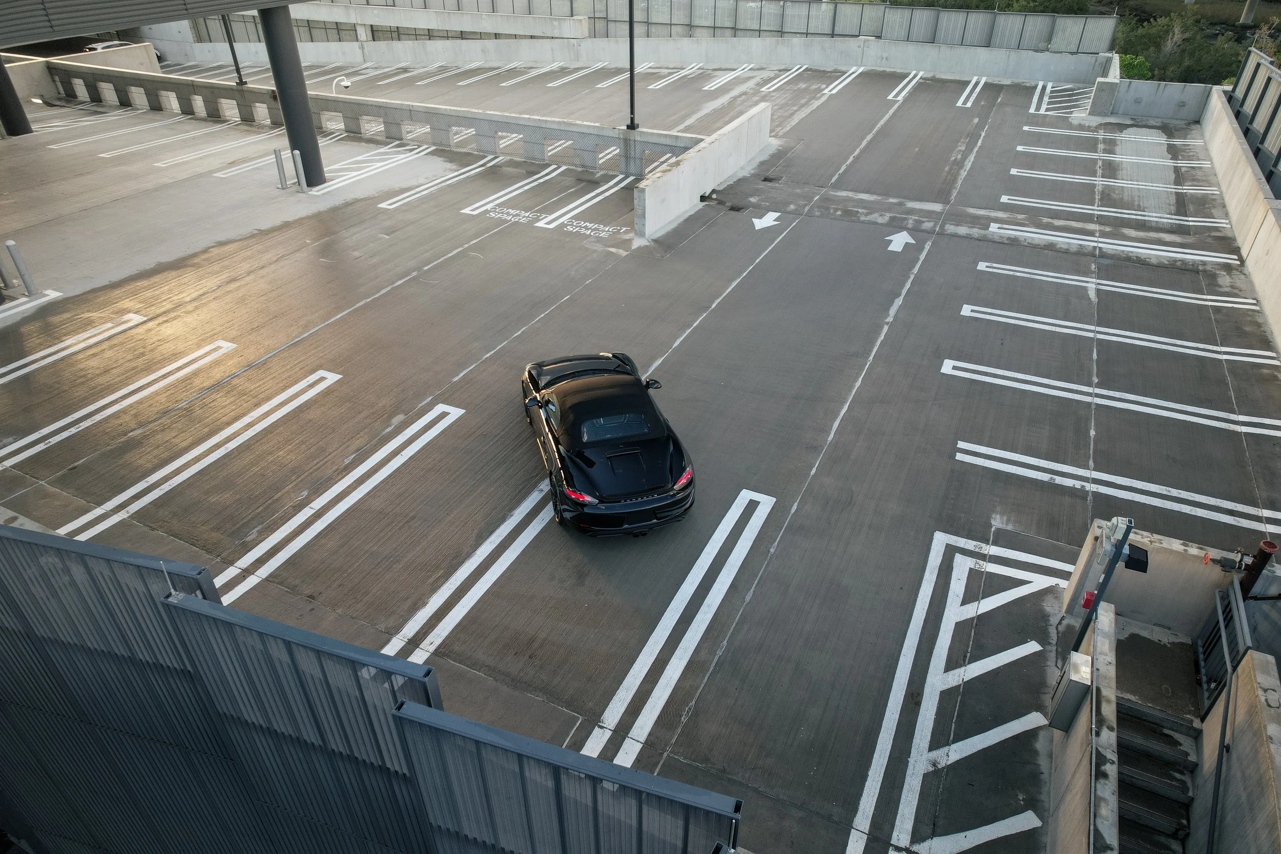 Empty multi-level parking garage with one black sports car parked in a space near the stairs.