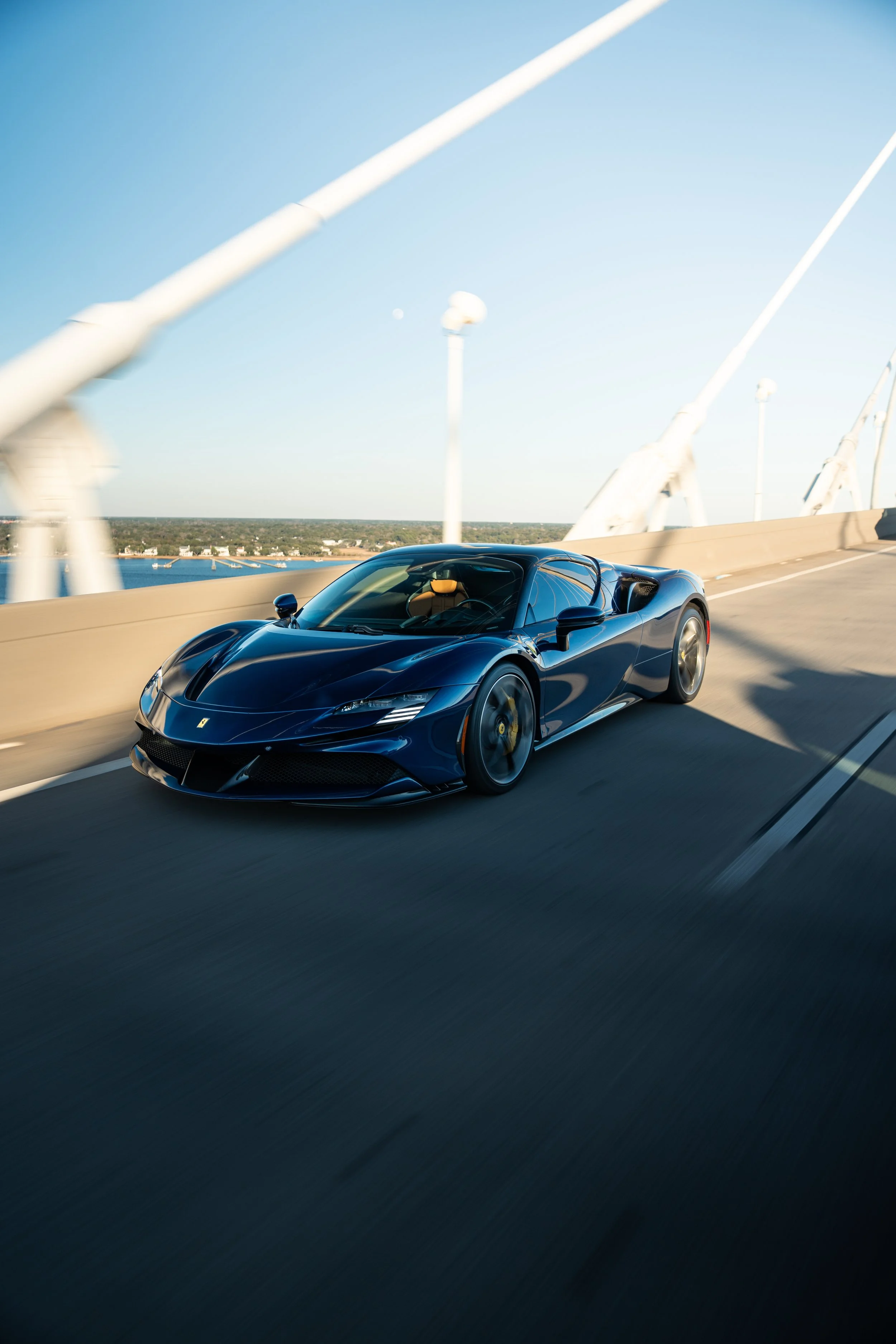 A sleek blue sports car driving on a bridge during daytime.