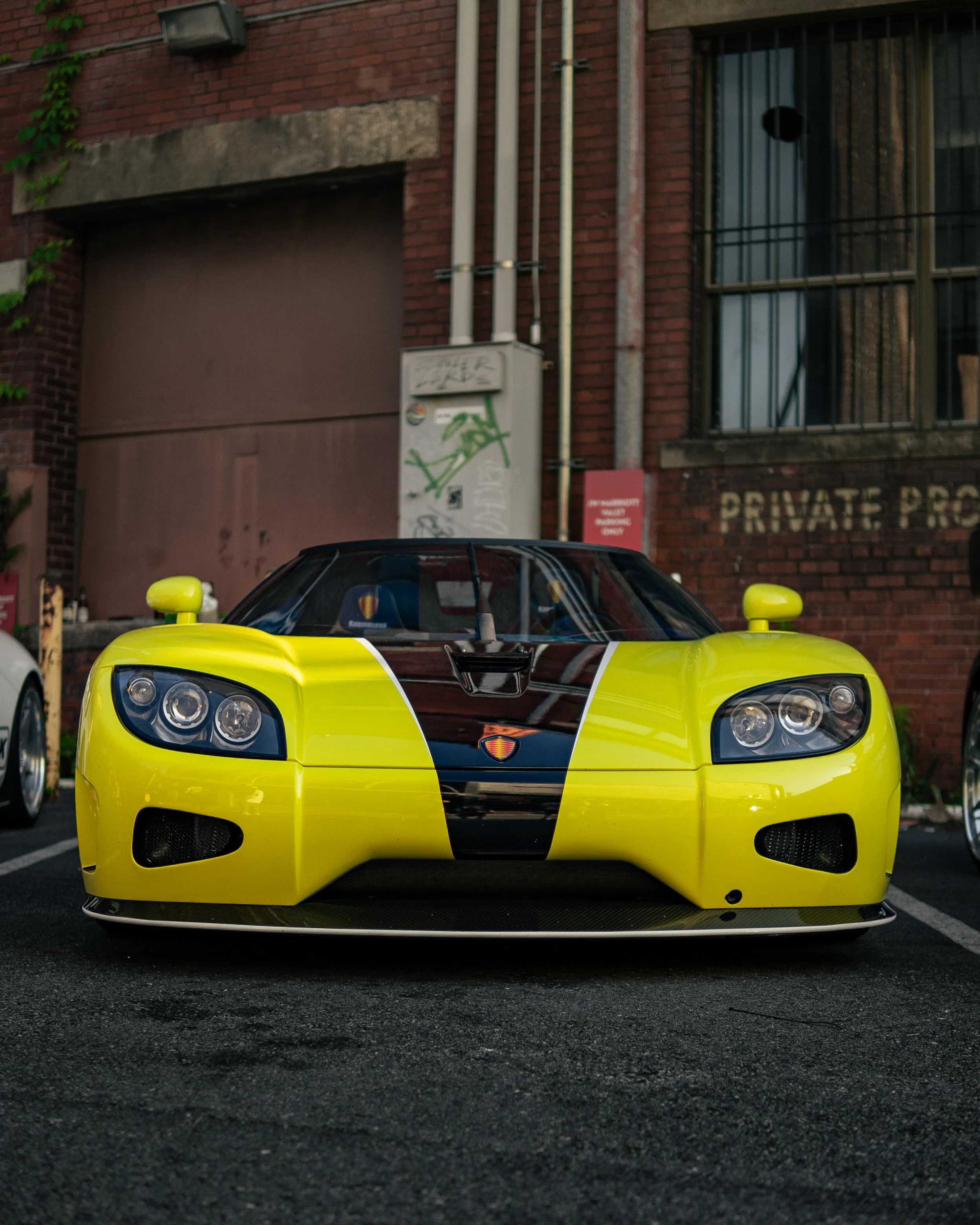 A yellow sports car with black and orange accents parked in front of a brick building.