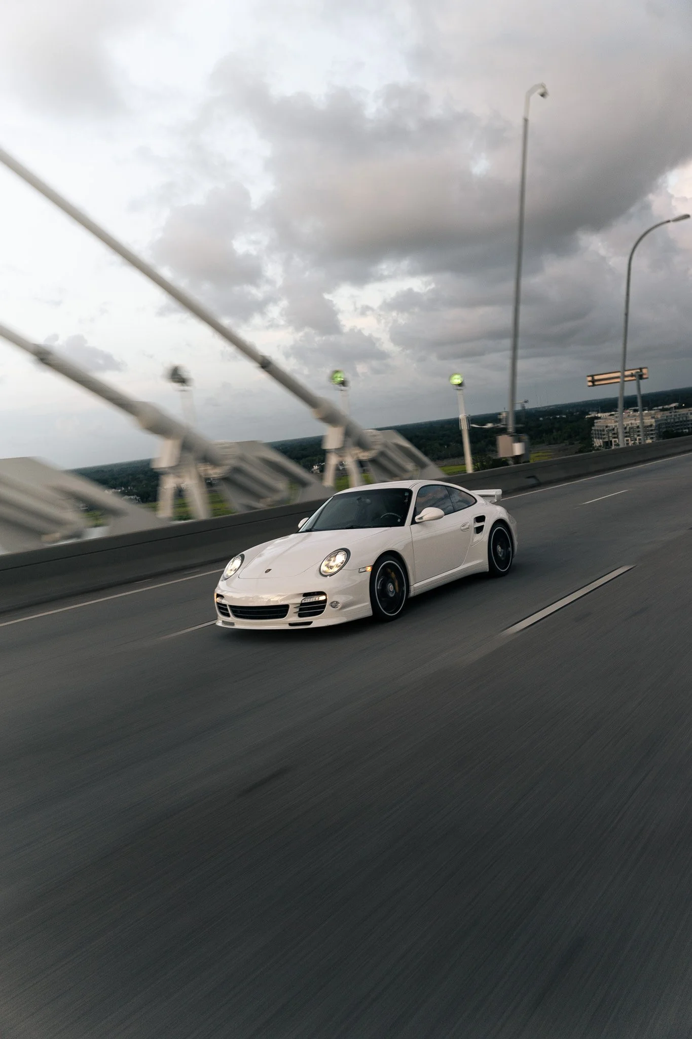 A white Porsche sports car driving on a highway with a cloudy sky above.