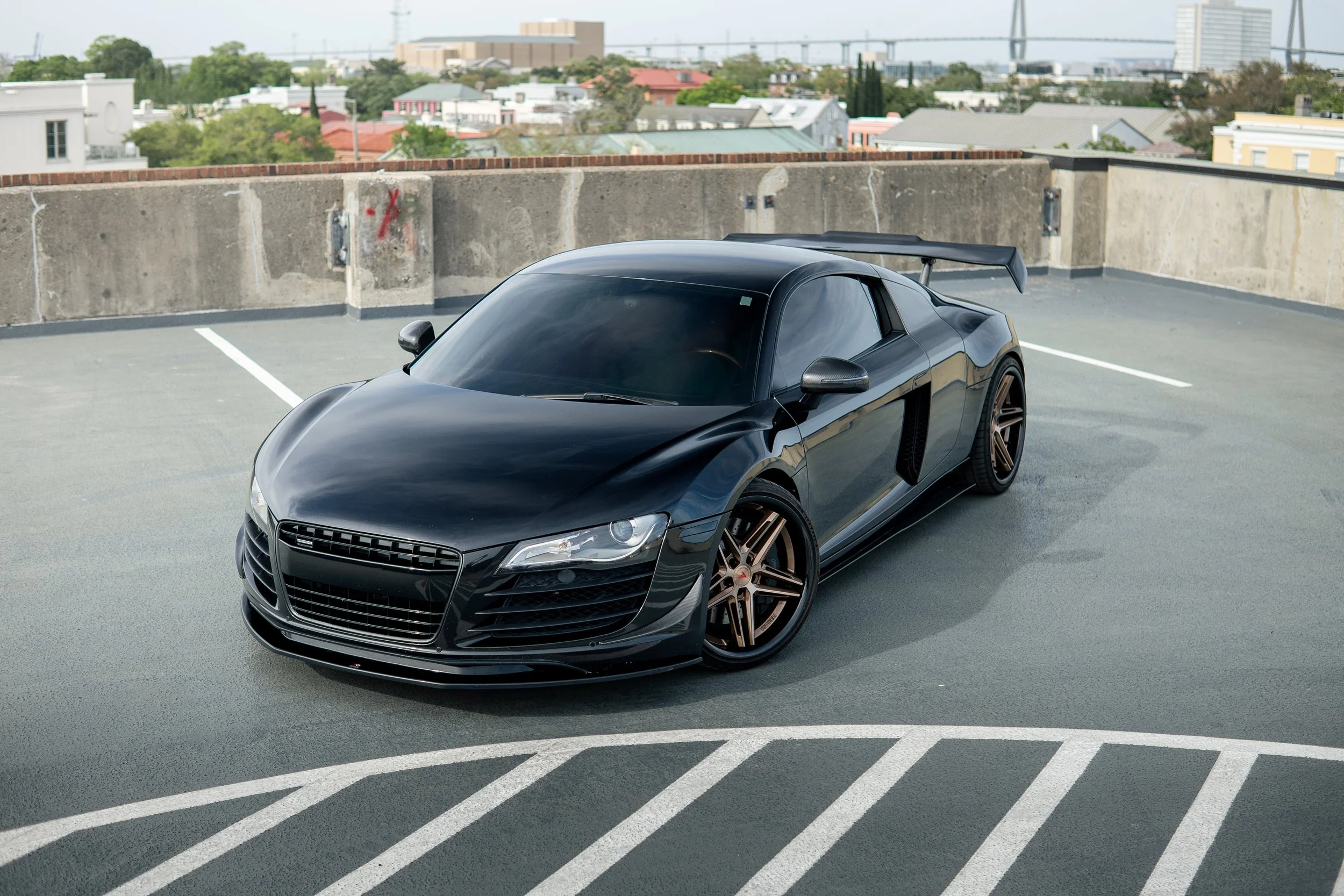 A black sports car with bronze wheels parked in a rooftop parking lot.