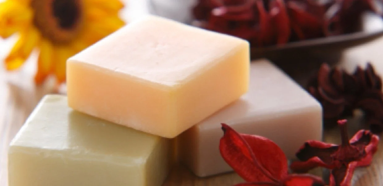 Three blocks of cheese in cream, white, and yellow colors on a wooden surface with dried red and yellow flowers in the background.