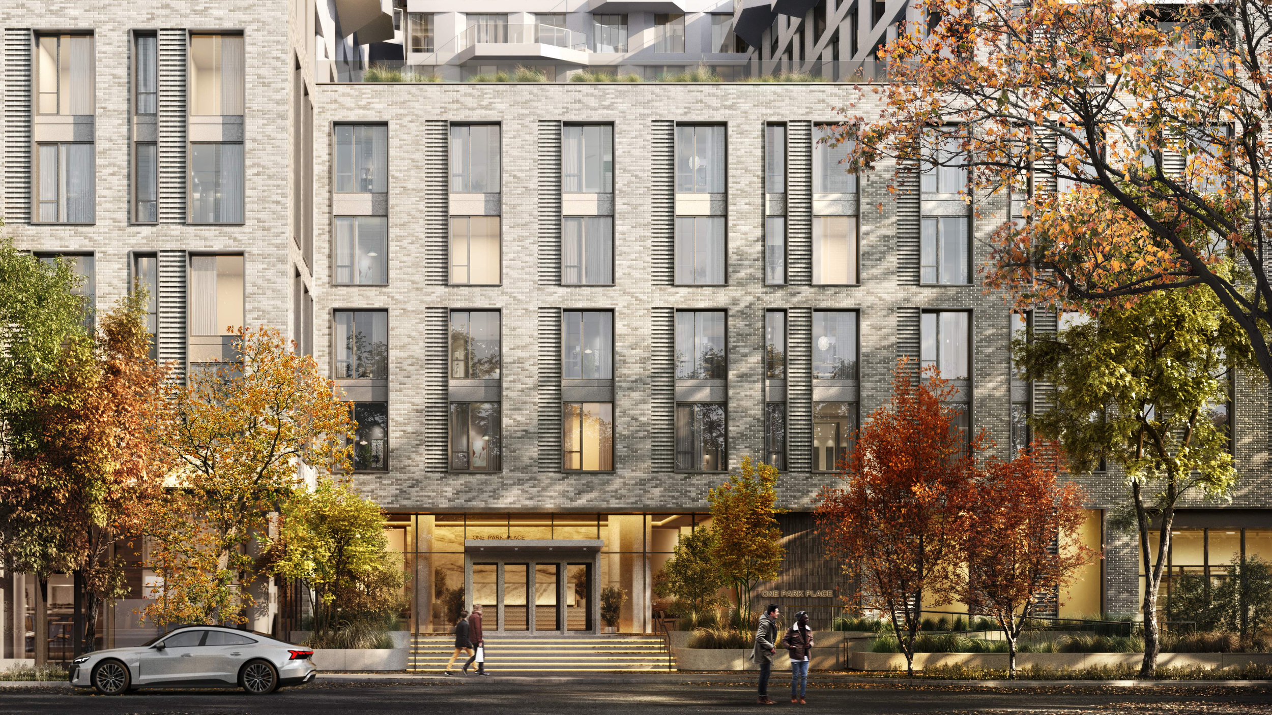 Modern multi-story building with large glass windows, surrounded by trees with fall foliage, and people walking on the sidewalk beneath, with a silver car parked in front