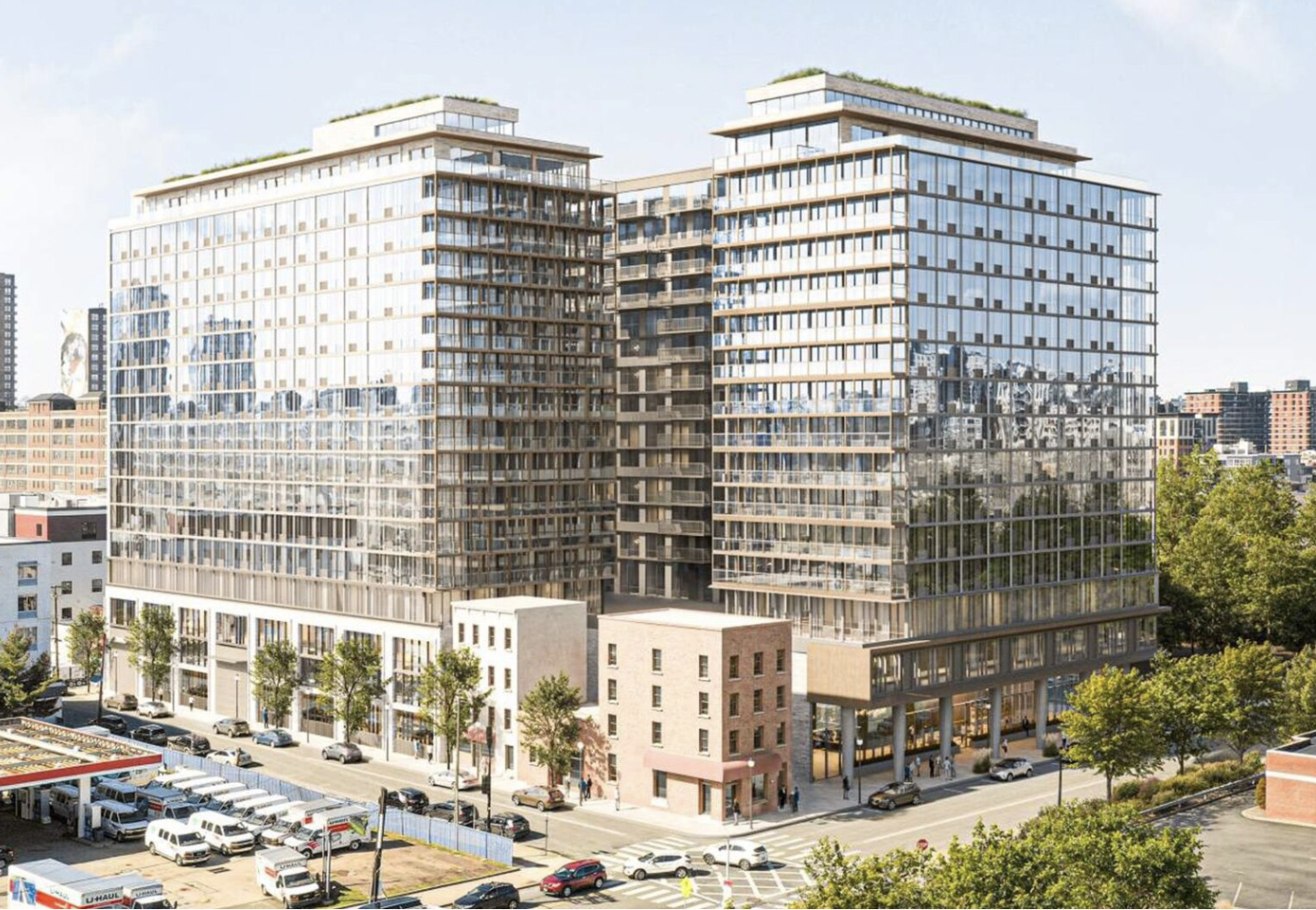 A modern multi-story hotel or office building with a glass exterior, reflecting the city skyline, situated on a city street with trees and parked cars.