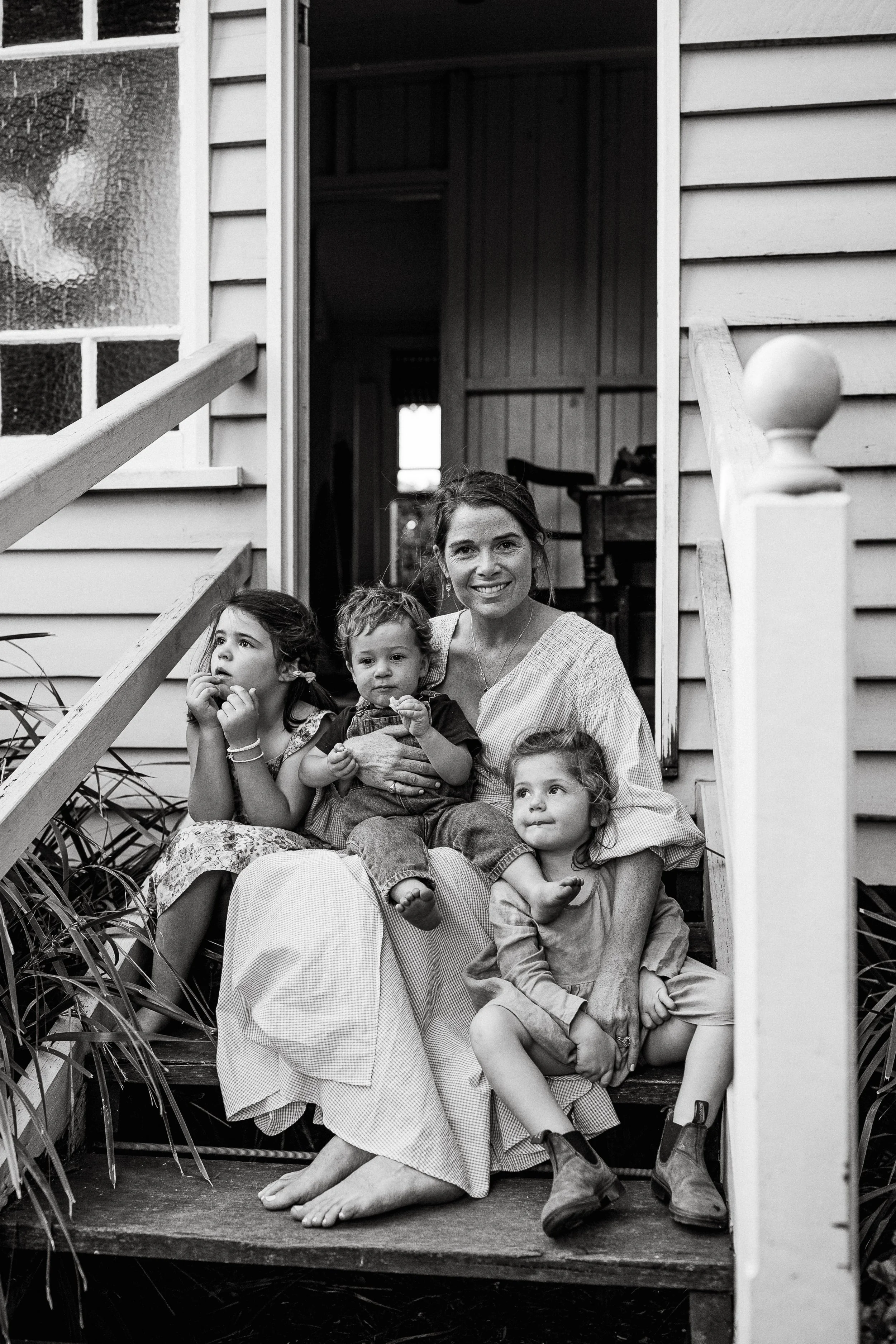 A black and white photo of a woman with three children sitting on the steps of a house.