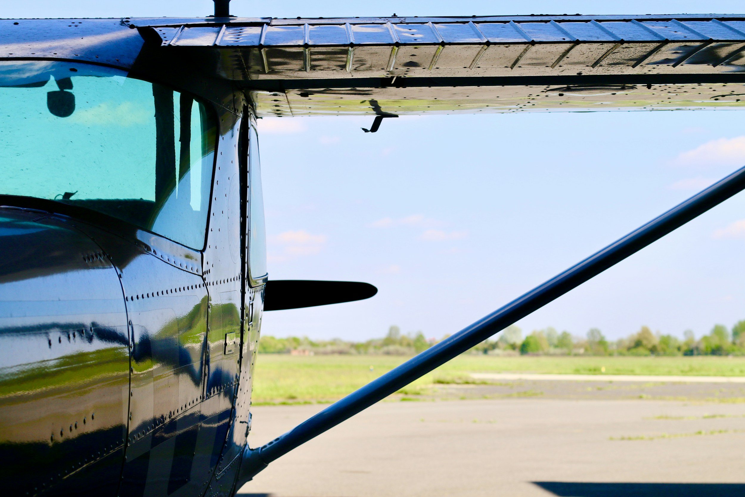 Close-up of a small airplane parked on an airfield with grass and trees in the background, taken during daytime.