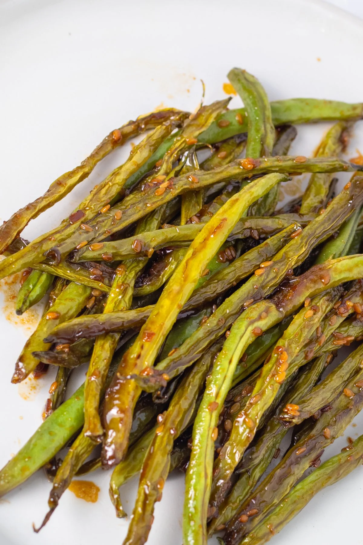 Roasted green beans with soy sauce and chili flakes on a white plate.