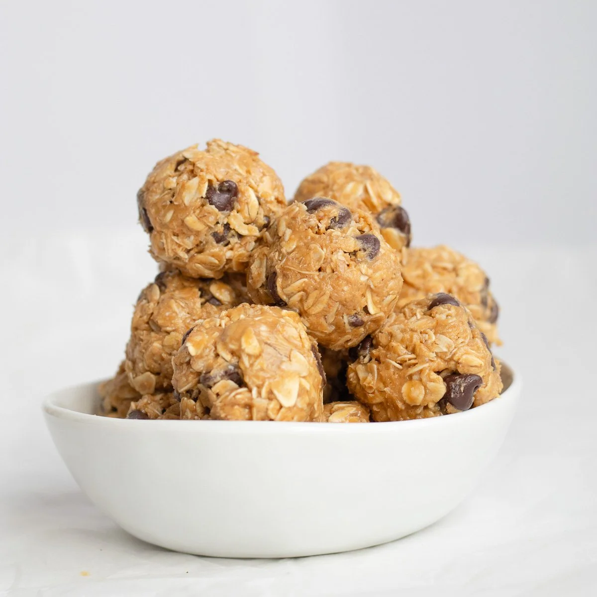 A white bowl filled with oatmeal energy bites containing oats and chocolate chips on a white background.