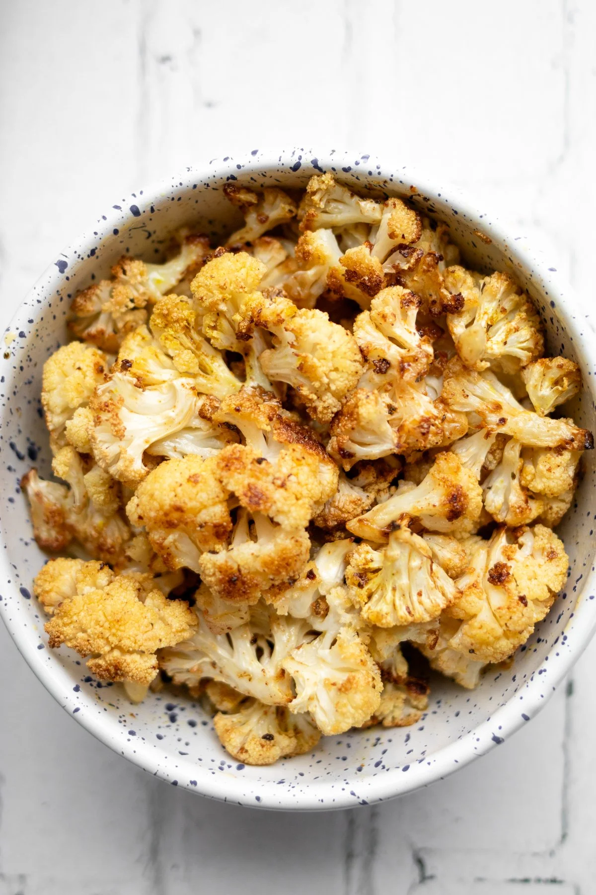 Roasted cauliflower in a speckled white bowl on a white surface.