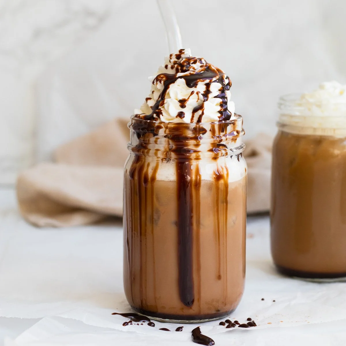 Chocolate milkshake topped with whipped cream and chocolate syrup in a glass jar, with a second jar of milkshake in the background.
