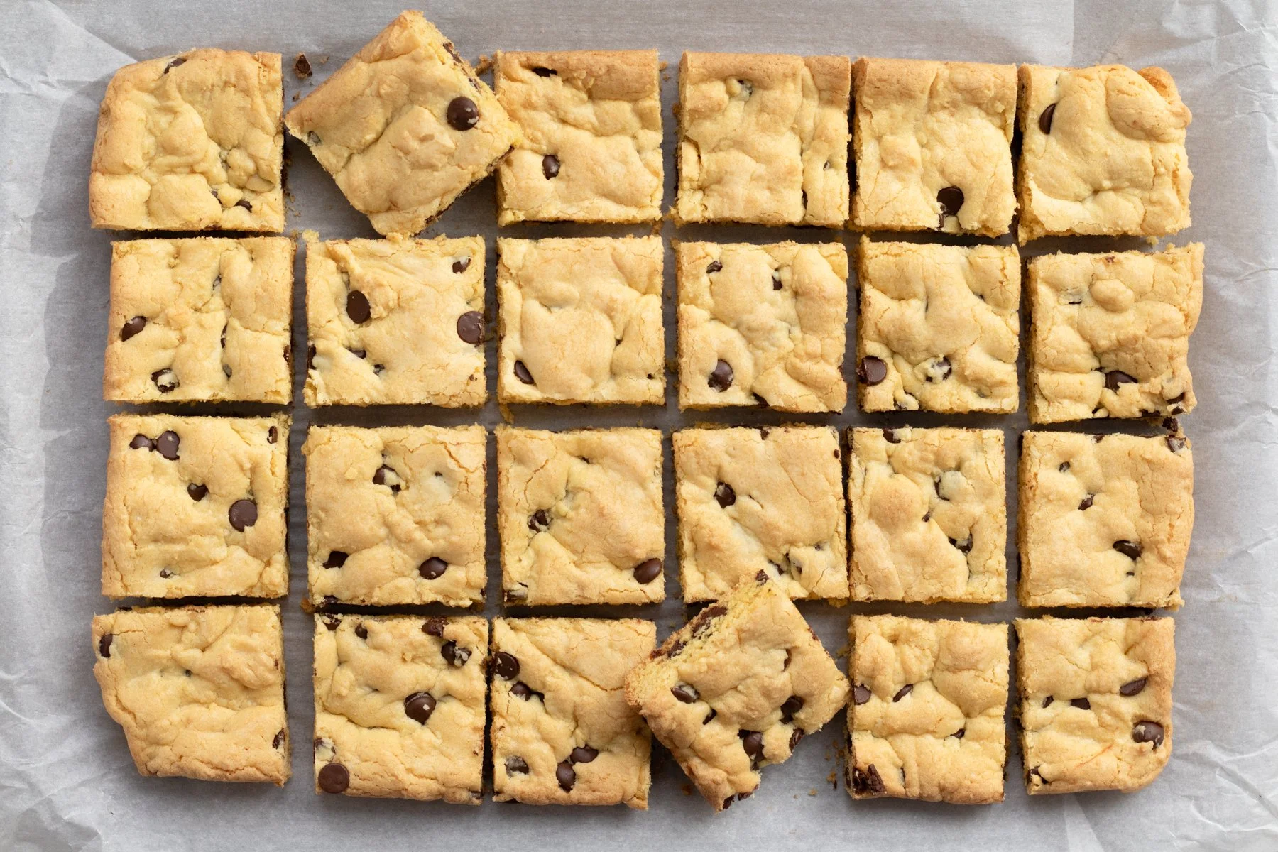 A tray of cut chocolate chip cookie bars on parchment paper, with some pieces slightly separated from the rest.