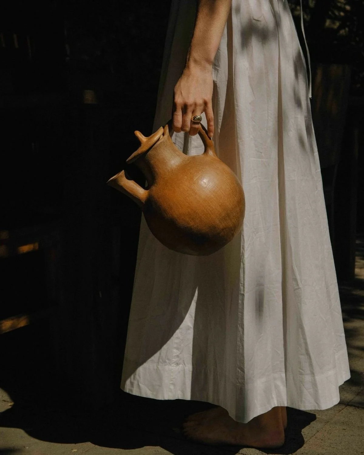 A person in a white dress is holding a wooden teapot by the handle.
