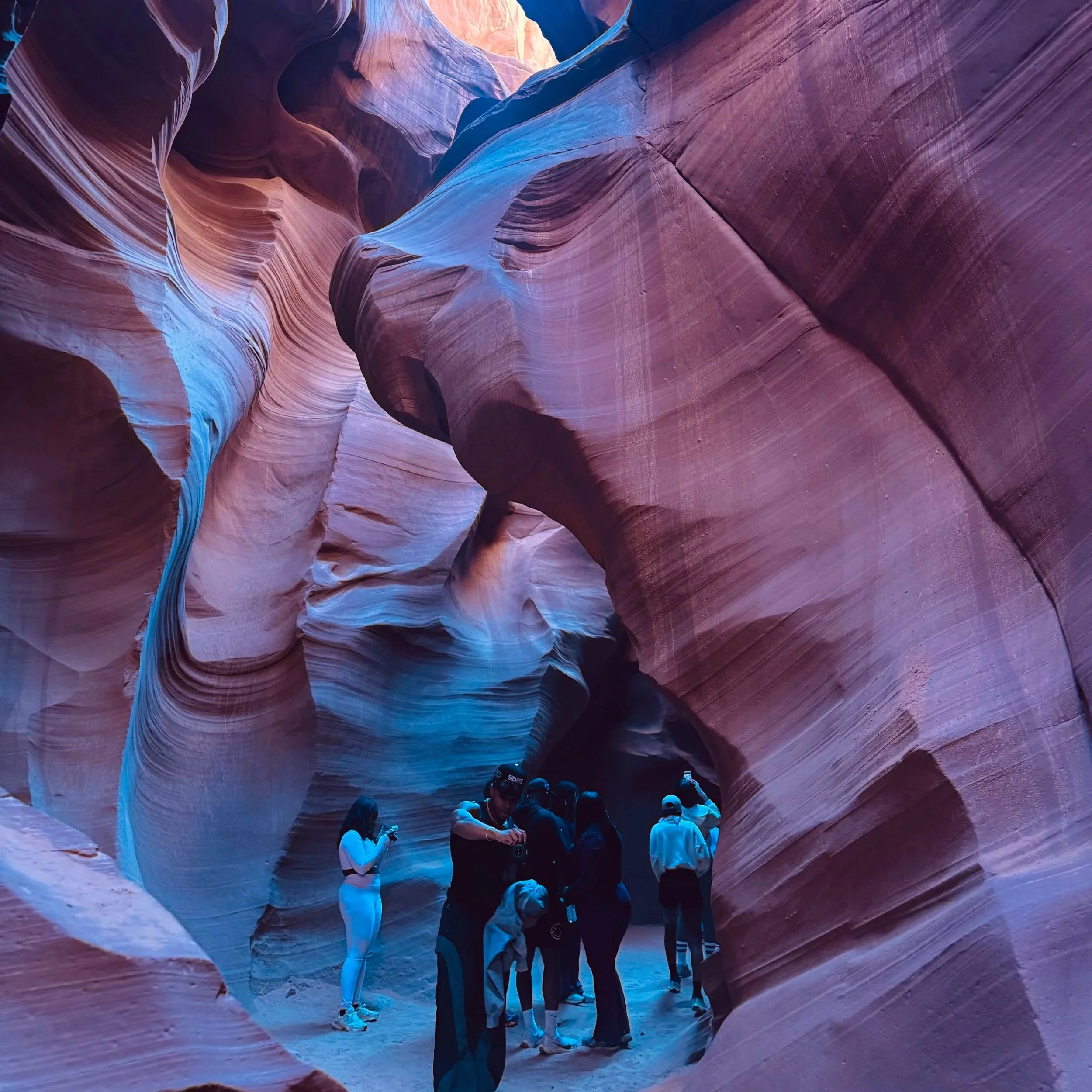 Group of people exploring a narrow slot canyon with smooth, curving walls in shades of red, purple, and blue