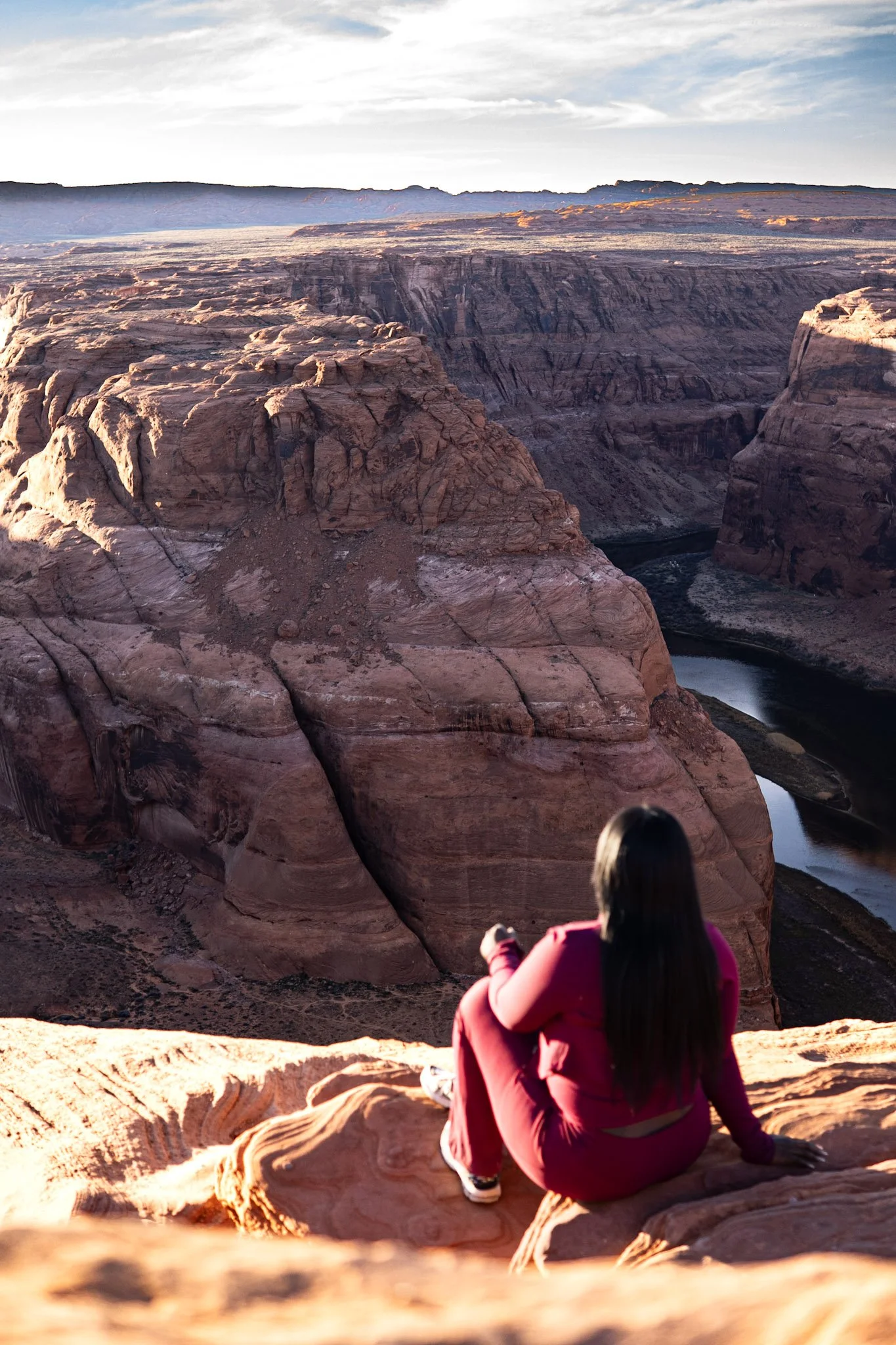 A woman in pink sitting on rock at Grand Canyon overlooking the canyon and Colorado River.