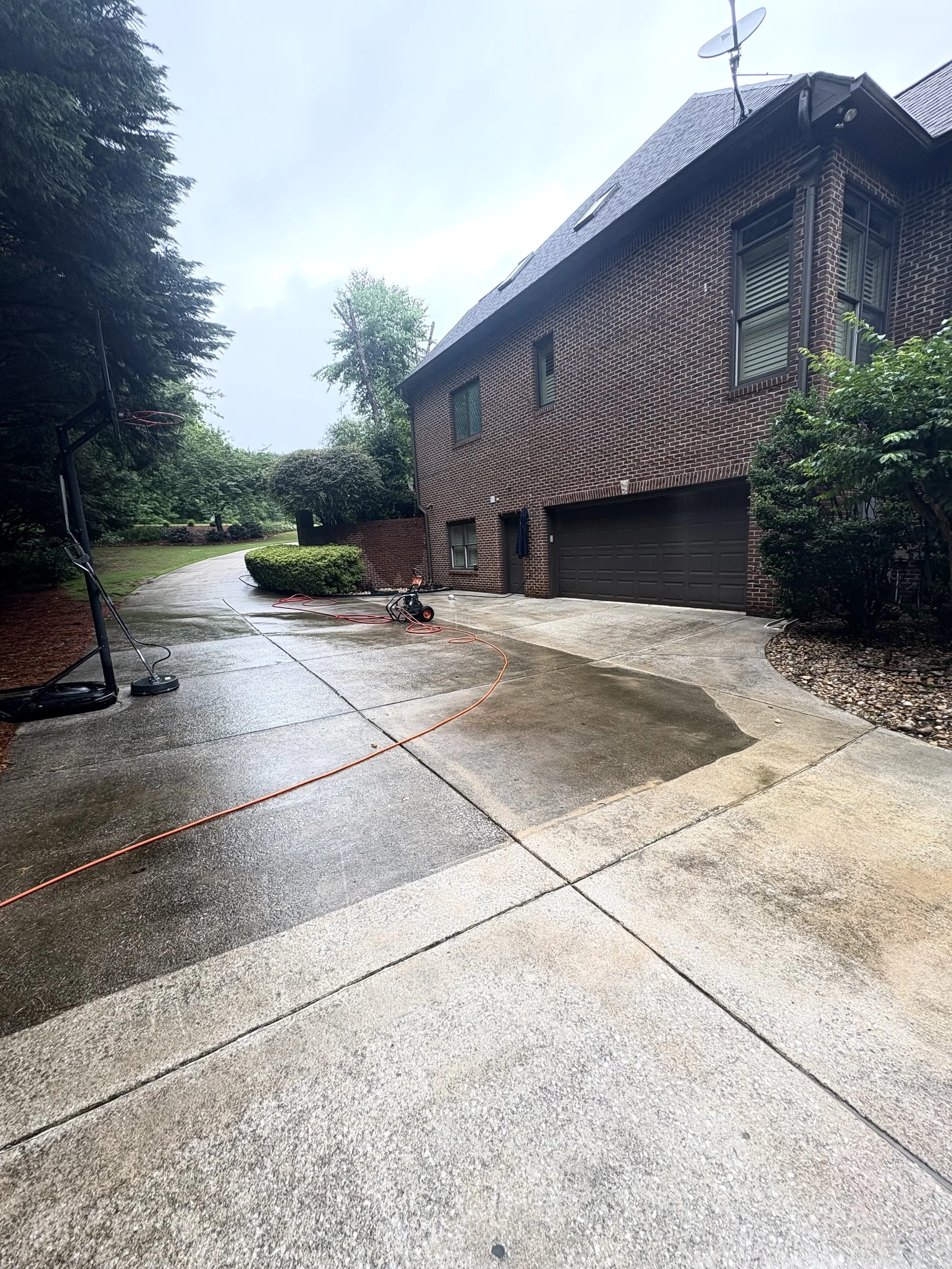 Wet driveway outside a brick house with a garage, two electric basketball hoops, and a pressure washer on the ground.