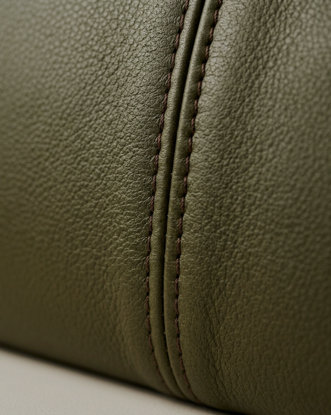 Close-up of green textured leather with brown stitching.