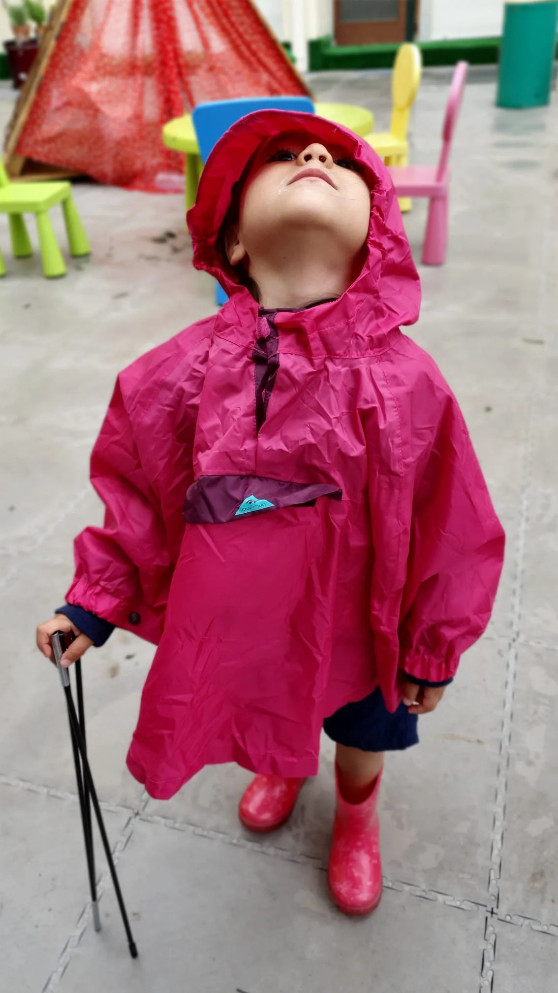 Girl in hot pink rain poncho looking up at the sky