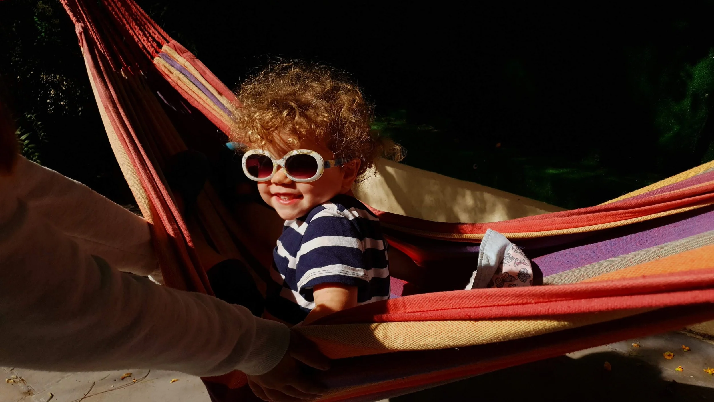Curly haired boy with sunglasses looking from a hammock