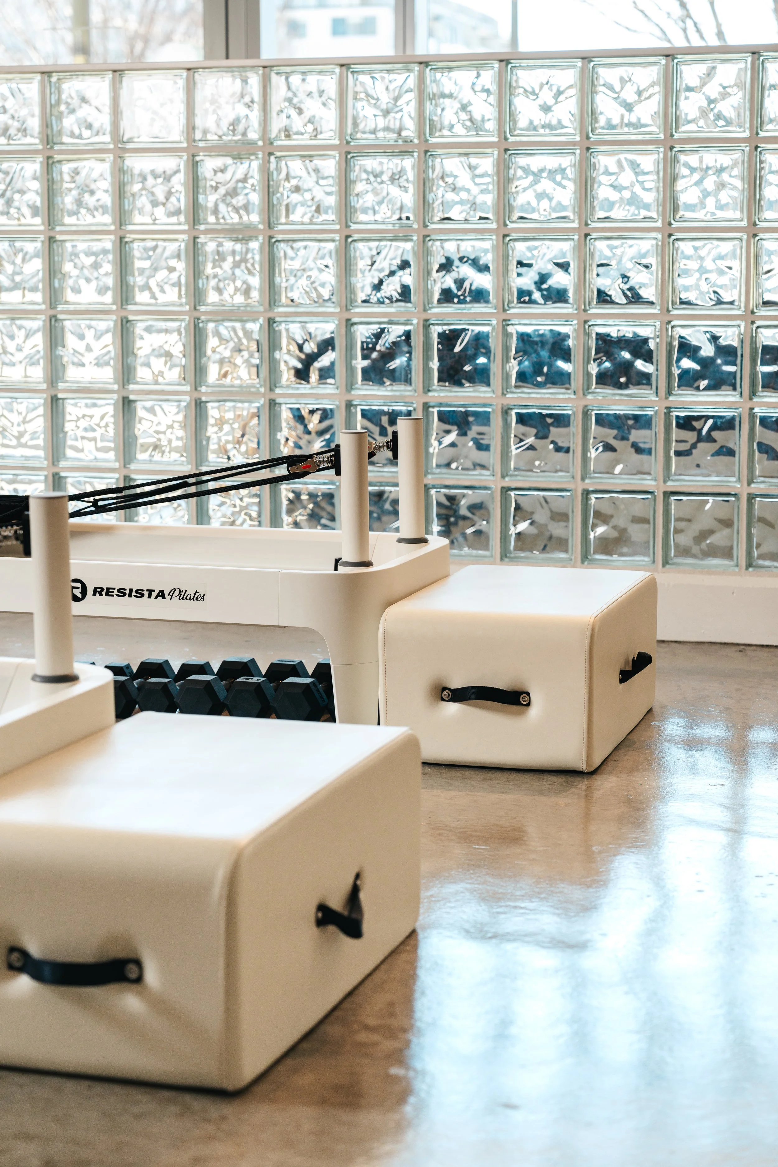 Pilates reformer machine in a bright fitness studio with large windows and glass block wall.