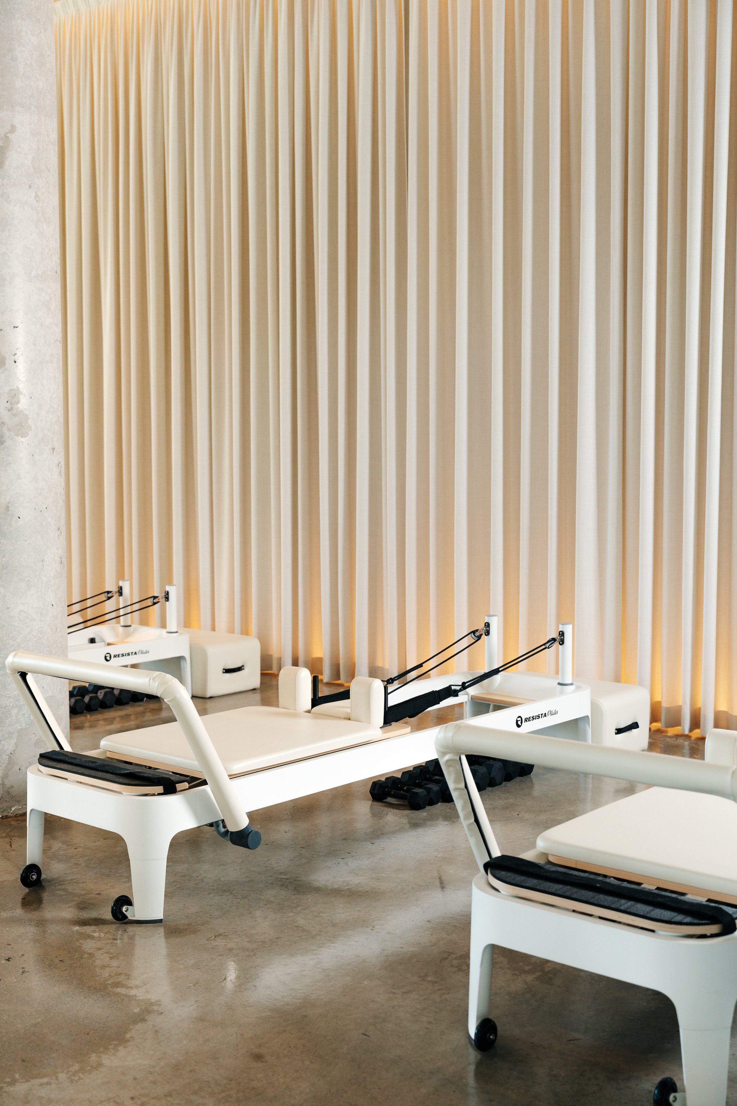 Reformer Pilates machine in a room with a beige curtain and a polished concrete floor.