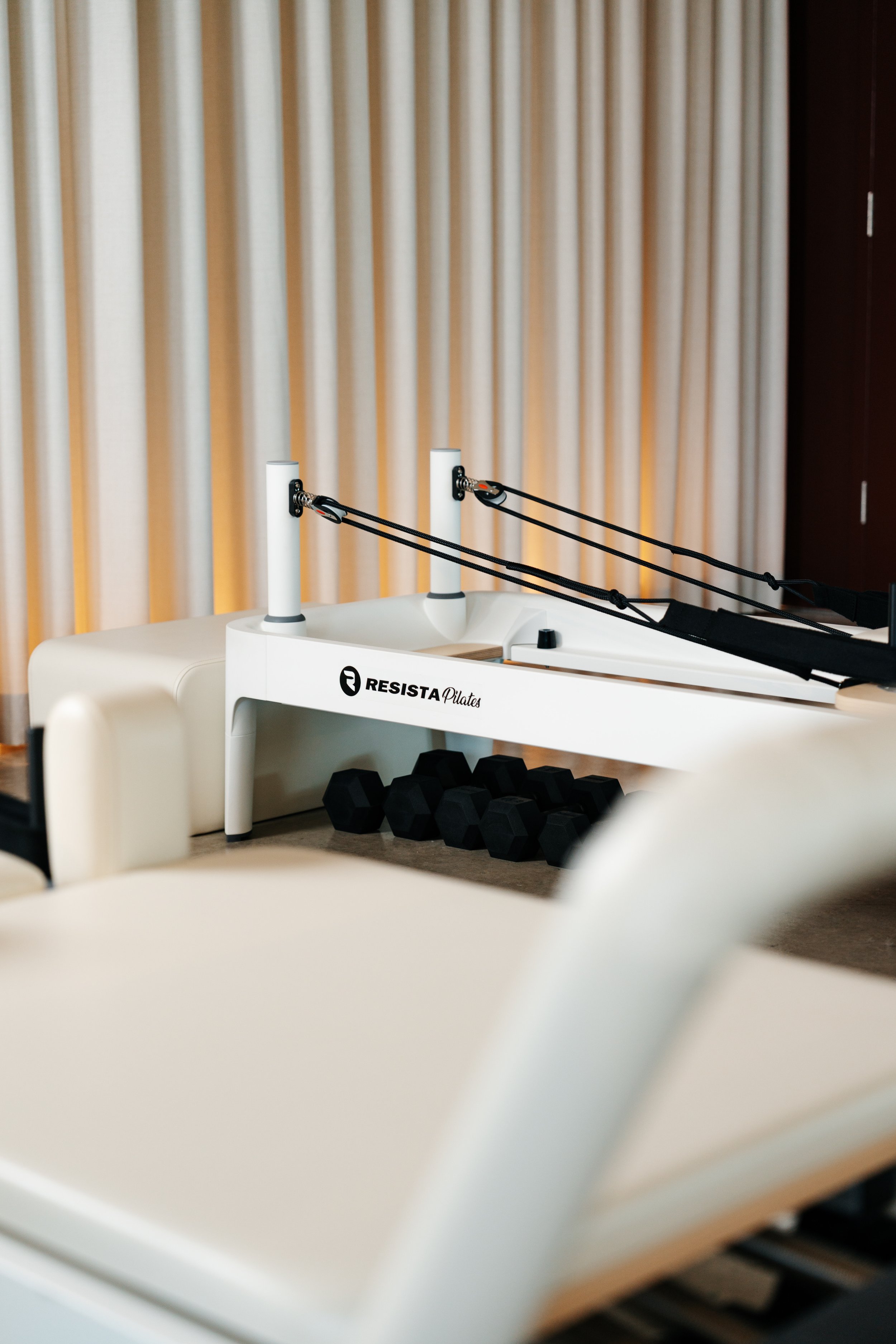 Pilates equipment with resistance bands, dumbbells, and a Pilates reformer machine in a studio with beige curtains.