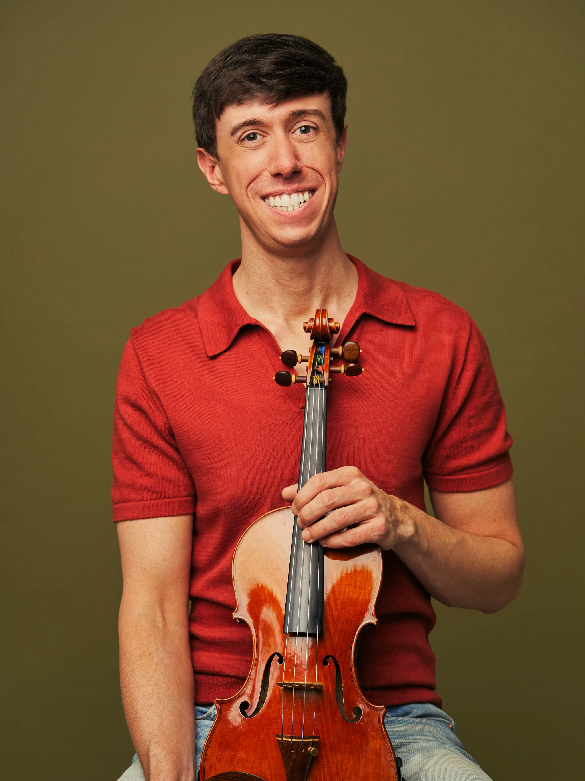 A man in a red short-sleeve shirt holding a violin.