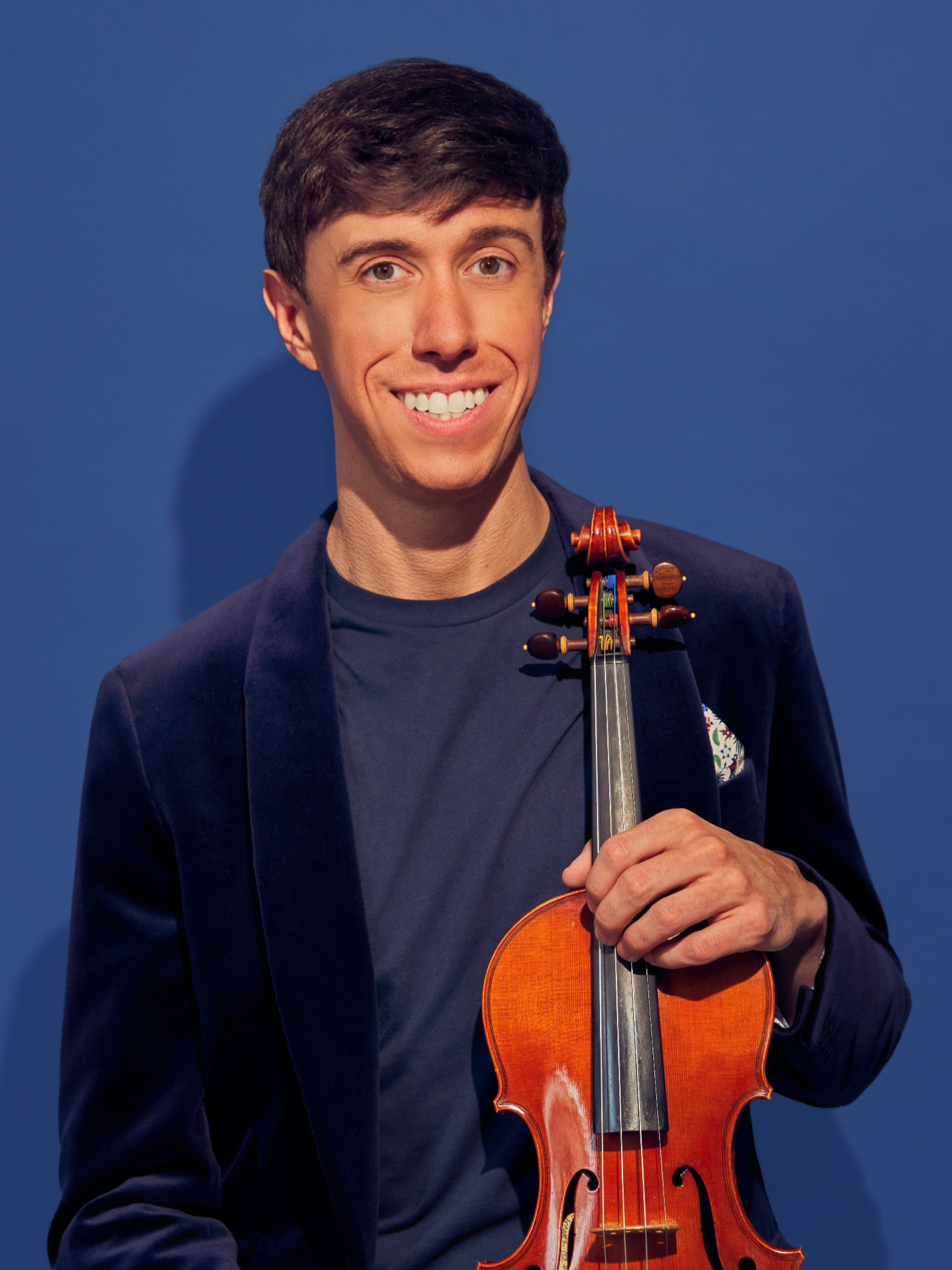 A smiling man holding a violin in front of a blue background.