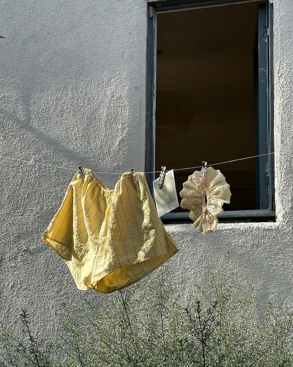 Yellow shorts, a cream scrunchie, and a photo clipped to a clothesline outside an open window.