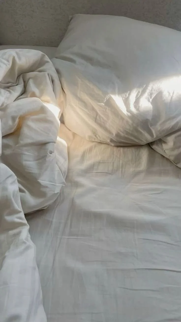 Unmade bed with white sheets, pillow, and comforter on a hotel bed.