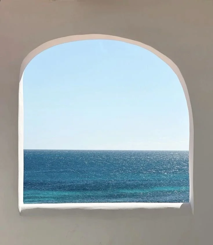 View of the ocean through an arched window with a white frame, clear blue sky above.