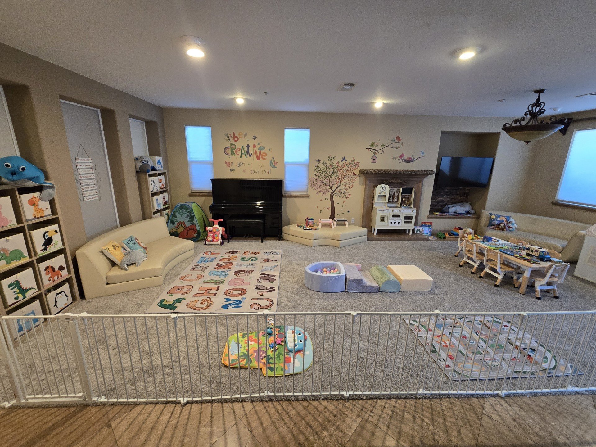 Child playroom with couches, toys, colorful rugs, and wall decorations, enclosed by a safety fence.