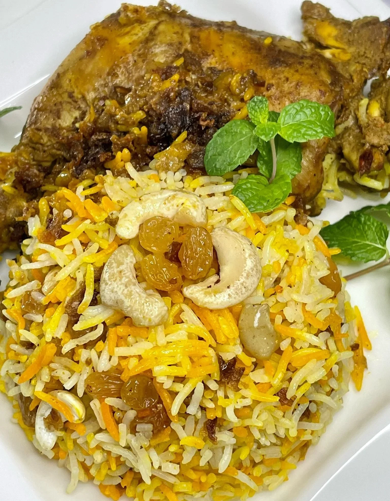 Plate of seasoned rice mixed with raisins and cashews, served with cooked meat garnished with fresh mint leaves.