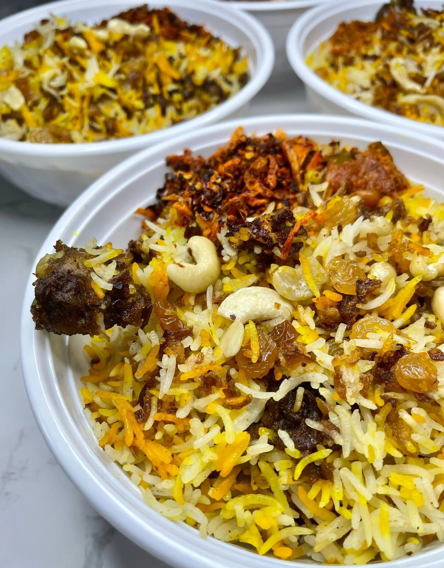 Close-up of bowls filled with colorful biryani rice with nuts, raisins, and meat