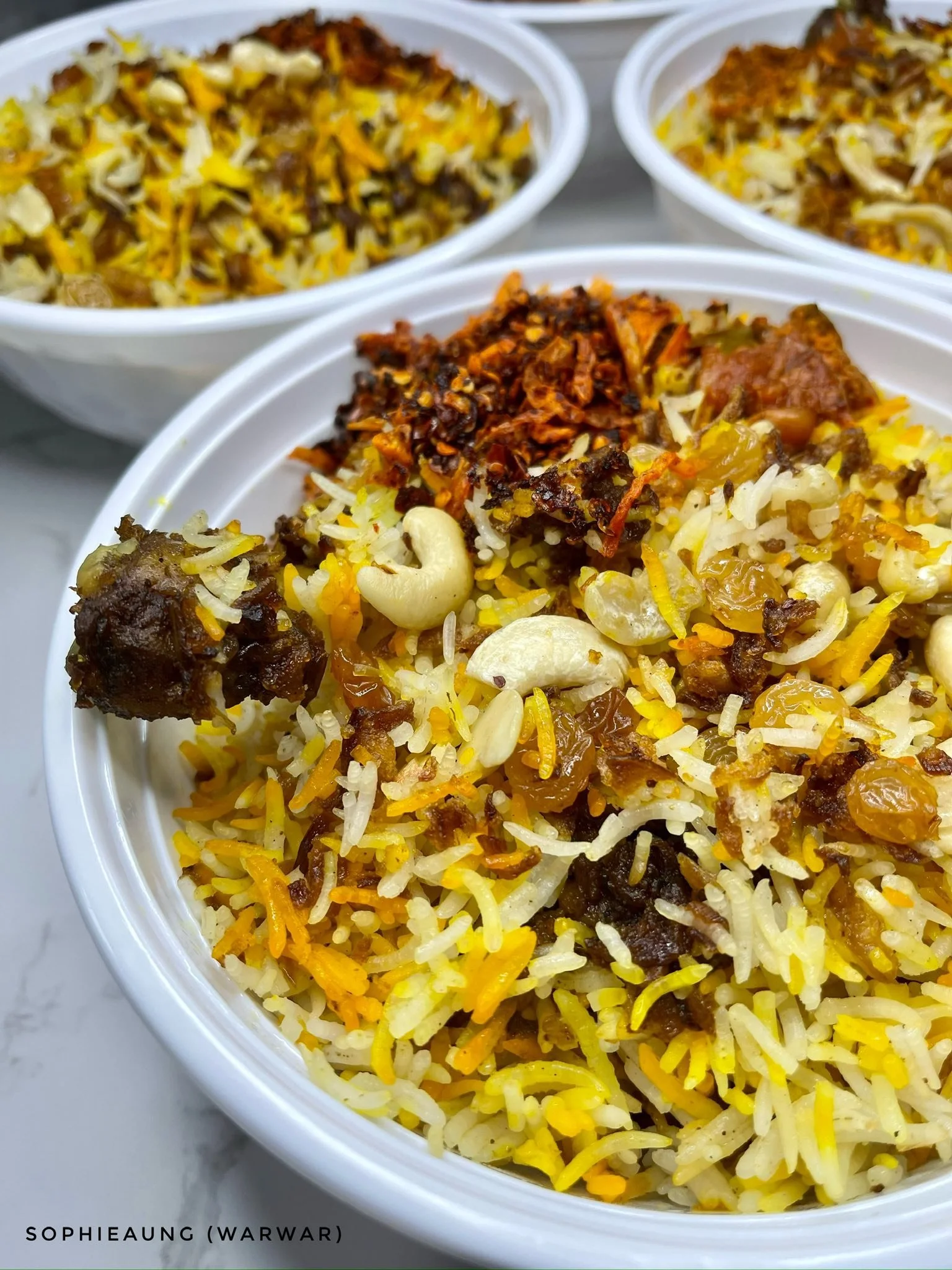 Close-up of bowls filled with biryani rice, featuring yellow and white rice mixed with nuts, raisins, and pieces of seasonings and spices.