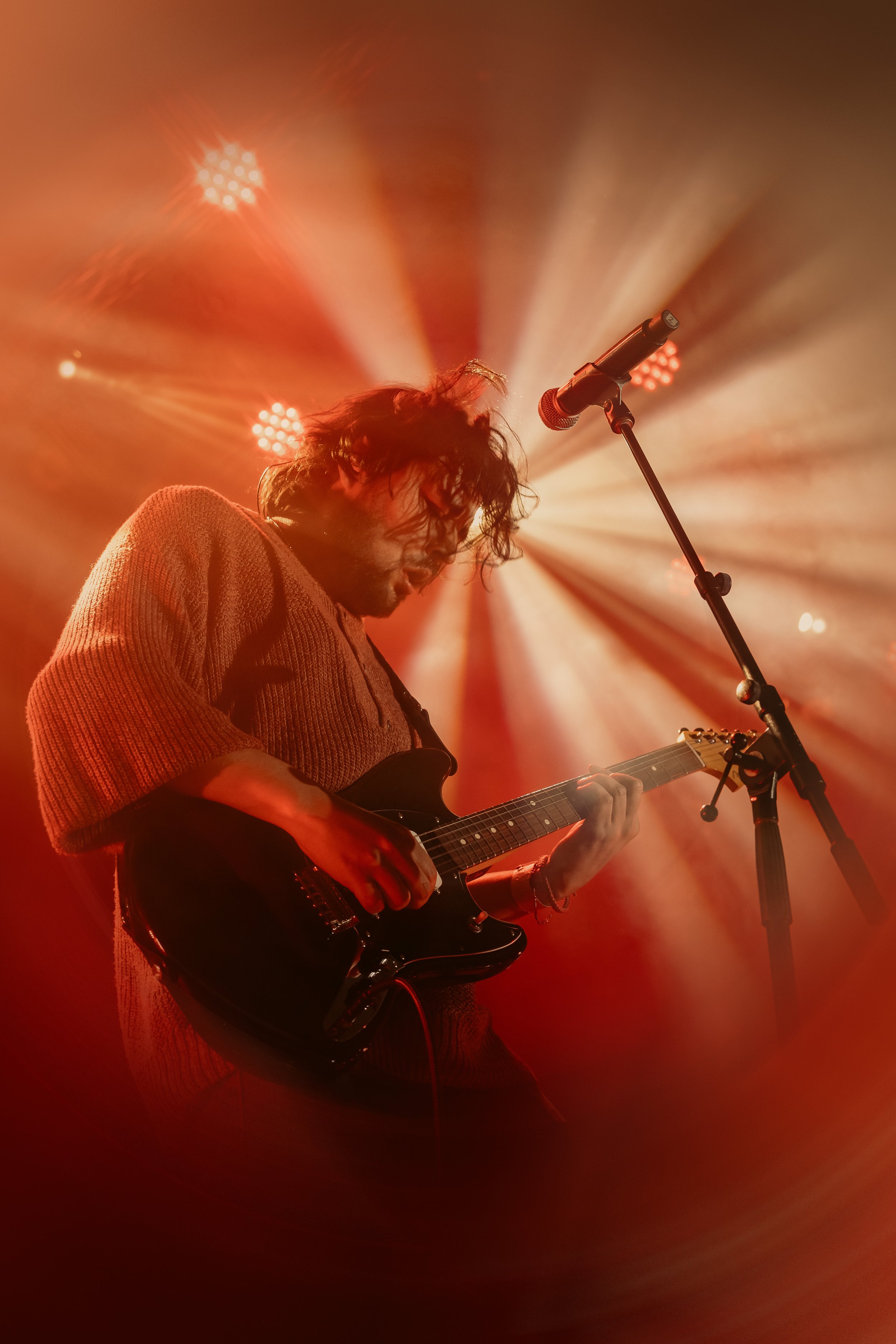 A musician playing an electric guitar on stage, illuminated by warm, colorful stage lights.