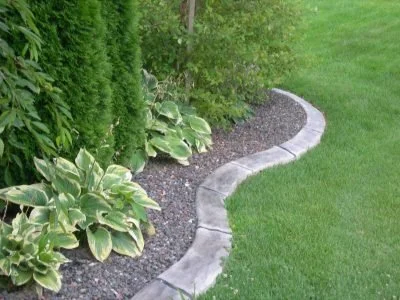 A curved garden bed with green plants, along a stone border on a grassy lawn.