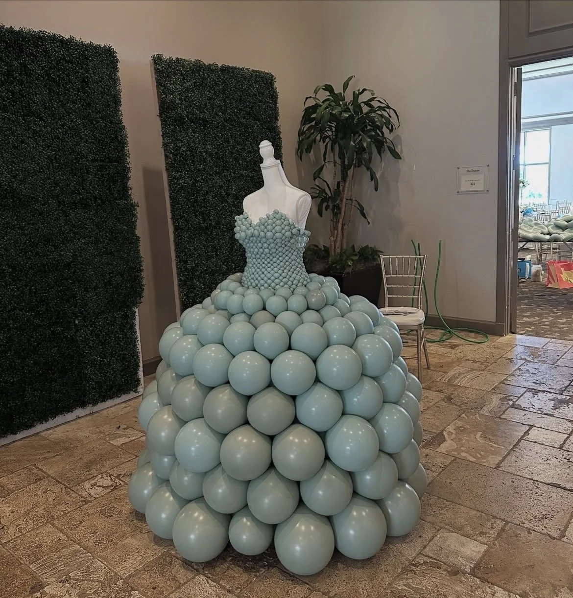 A dress made of light blue balloons with a fitted bodice and full skirt, displayed on a mannequin in an indoor setting.