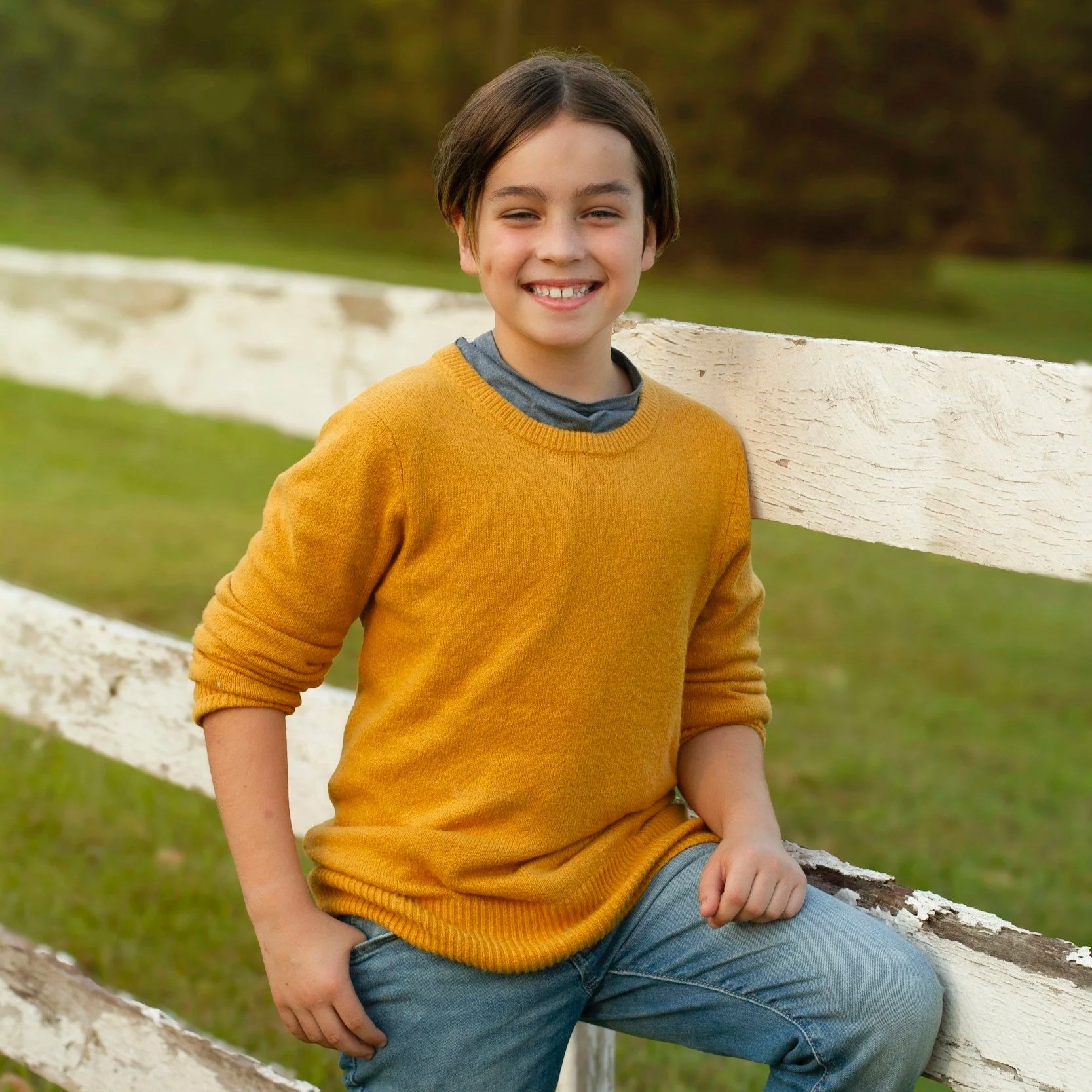 A smiling boy poses for a portrait outdoors.