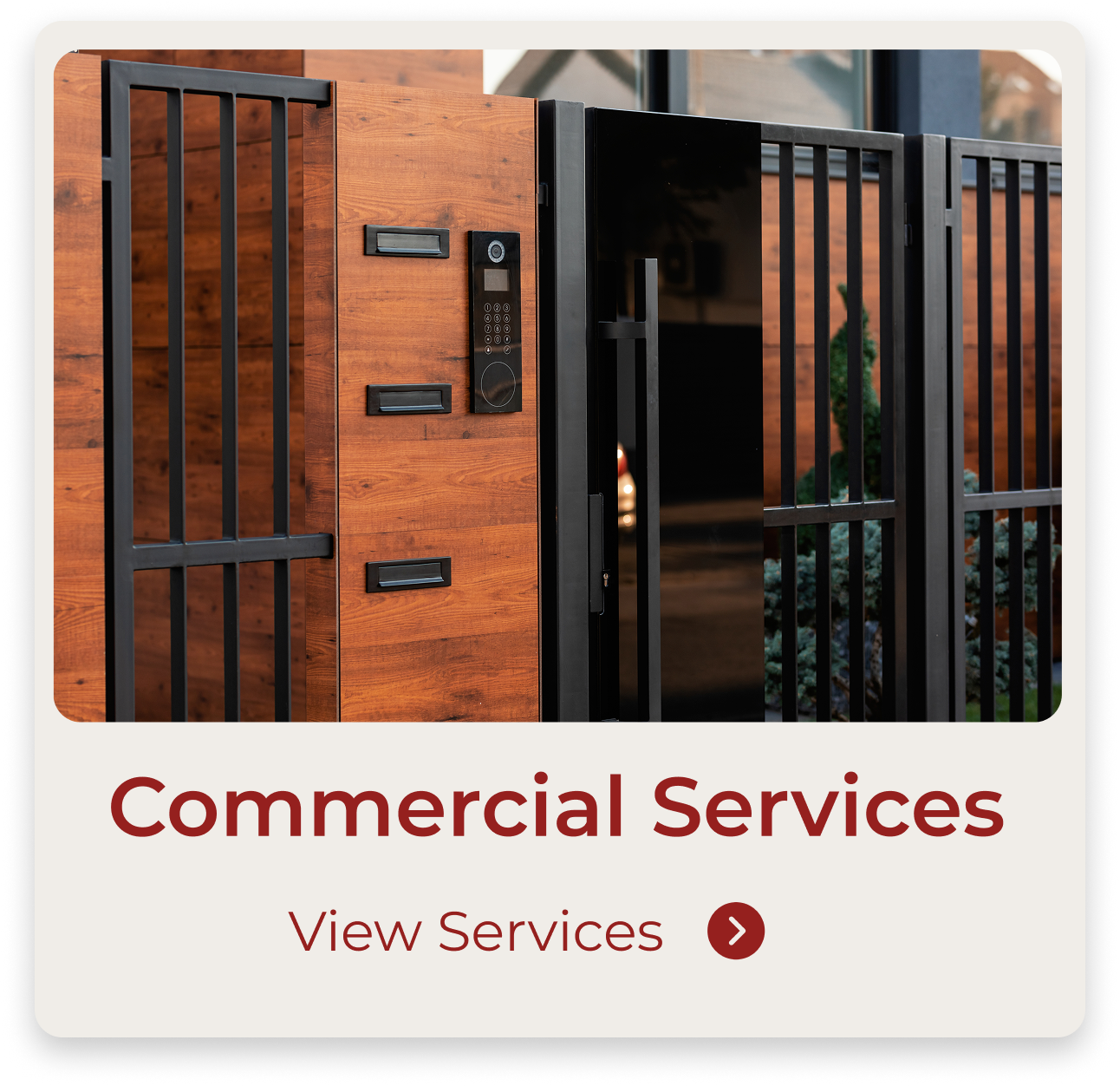Close-up of a modern black gate with intercom system and mailbox attached, part of a wooden fence with a house reflected in the windows behind.