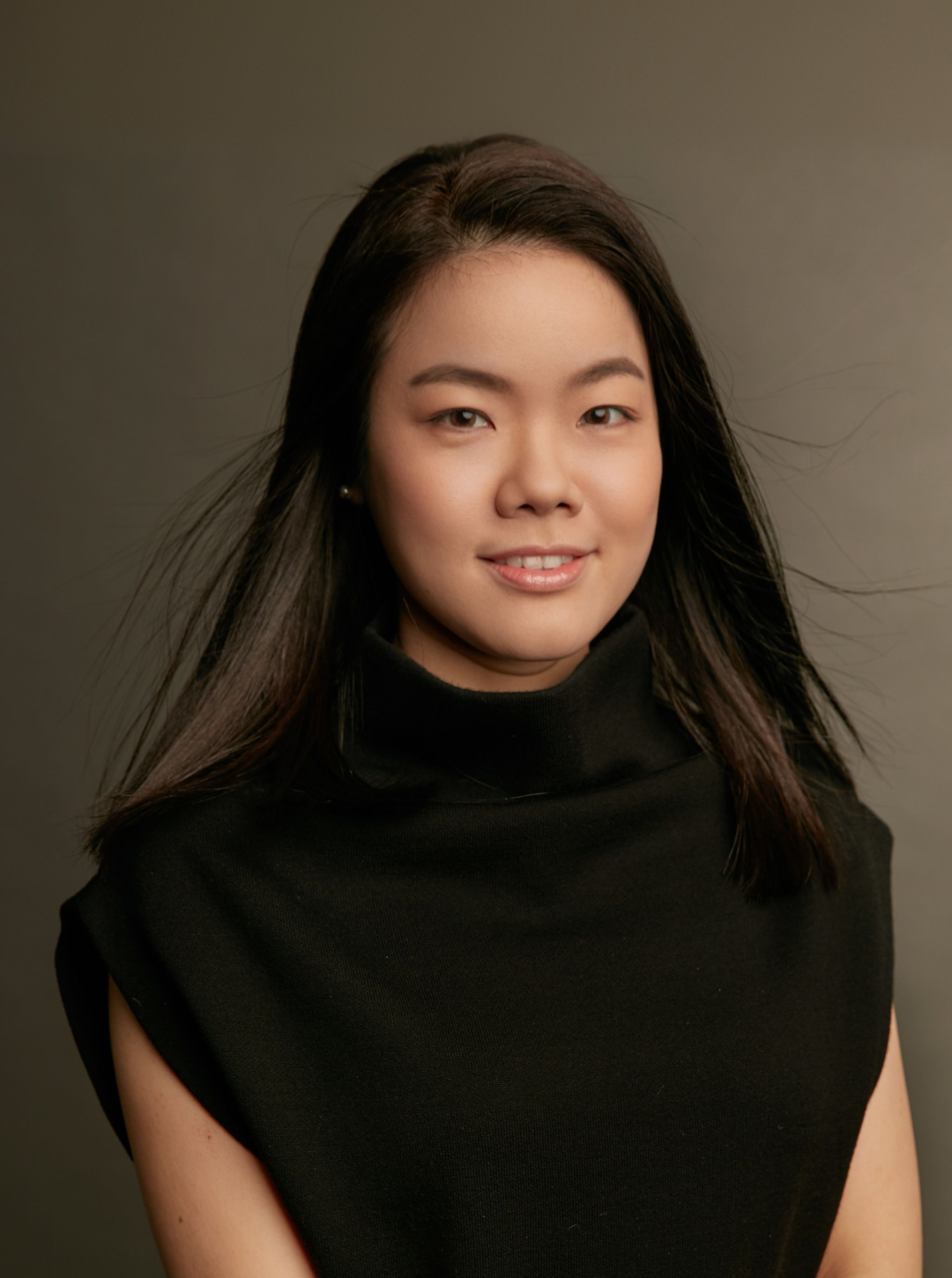 一名年輕亞洲女性的肖像，她留著一頭烏黑長髮，身穿黑色無袖上衣，面帶微笑，背景為素雅的灰色。