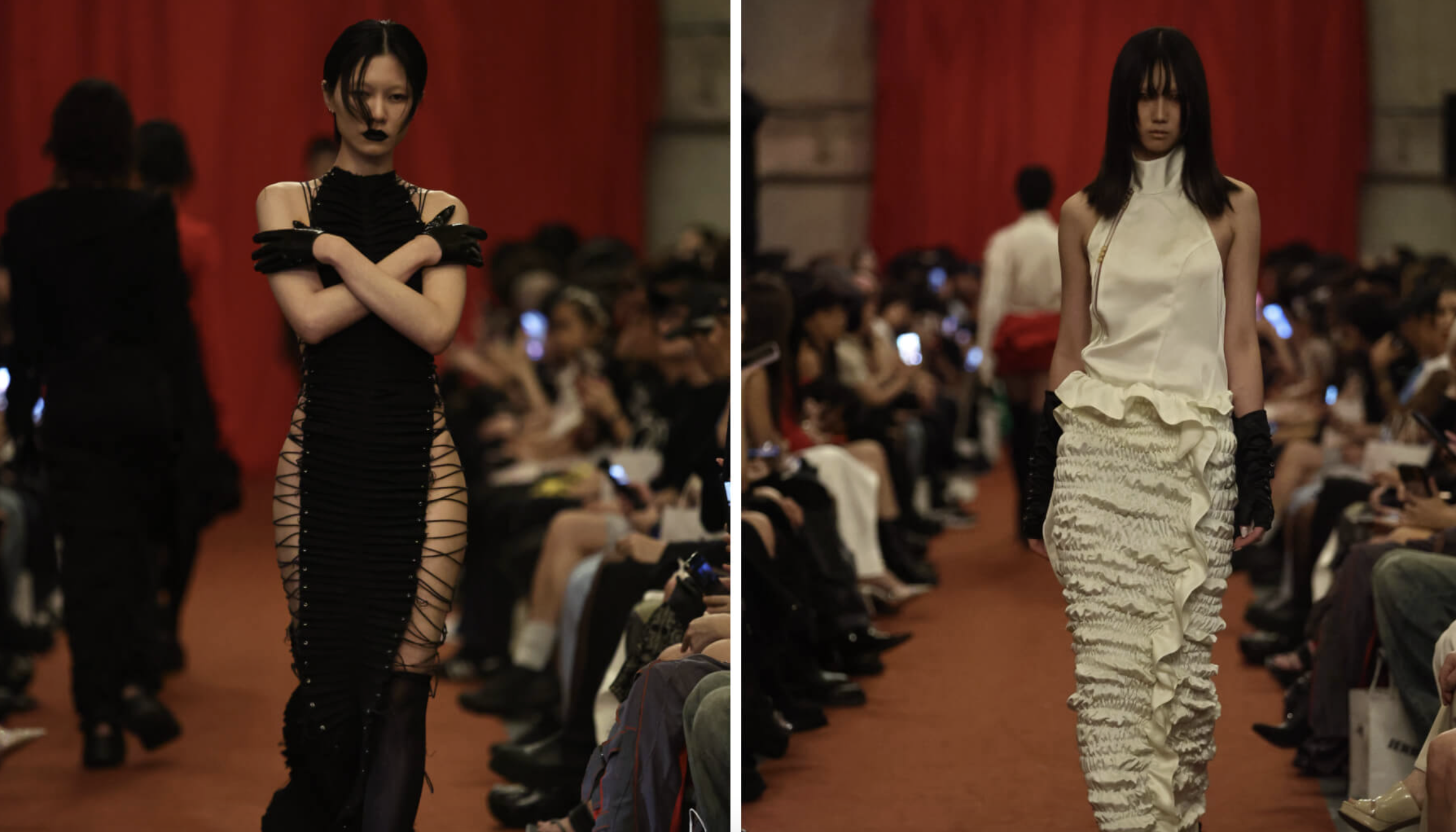 Two female models walking down a runway during a fashion show in front of an audience, with red curtains in the background.
