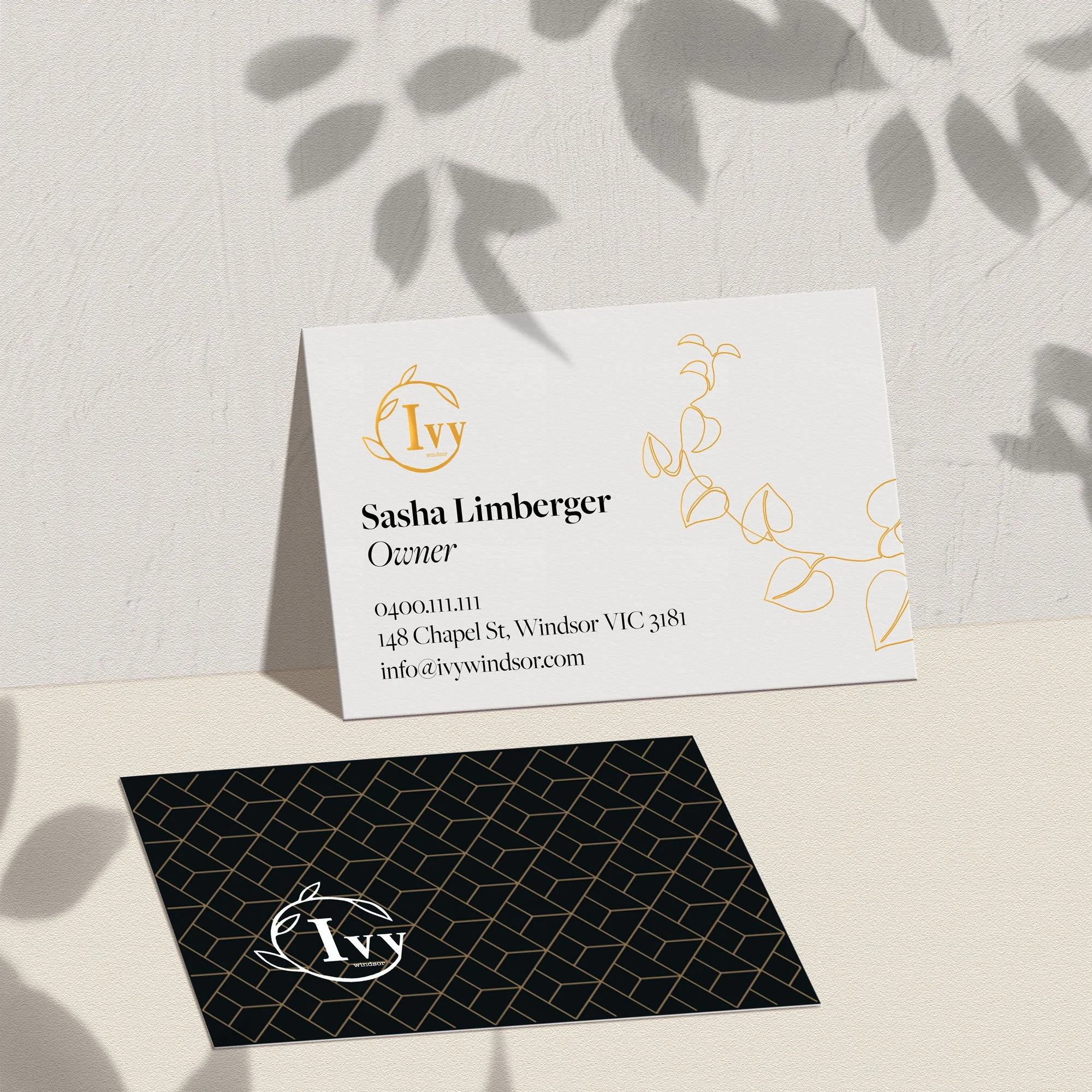 Business card showing front with gold ivy design element and black patterned back